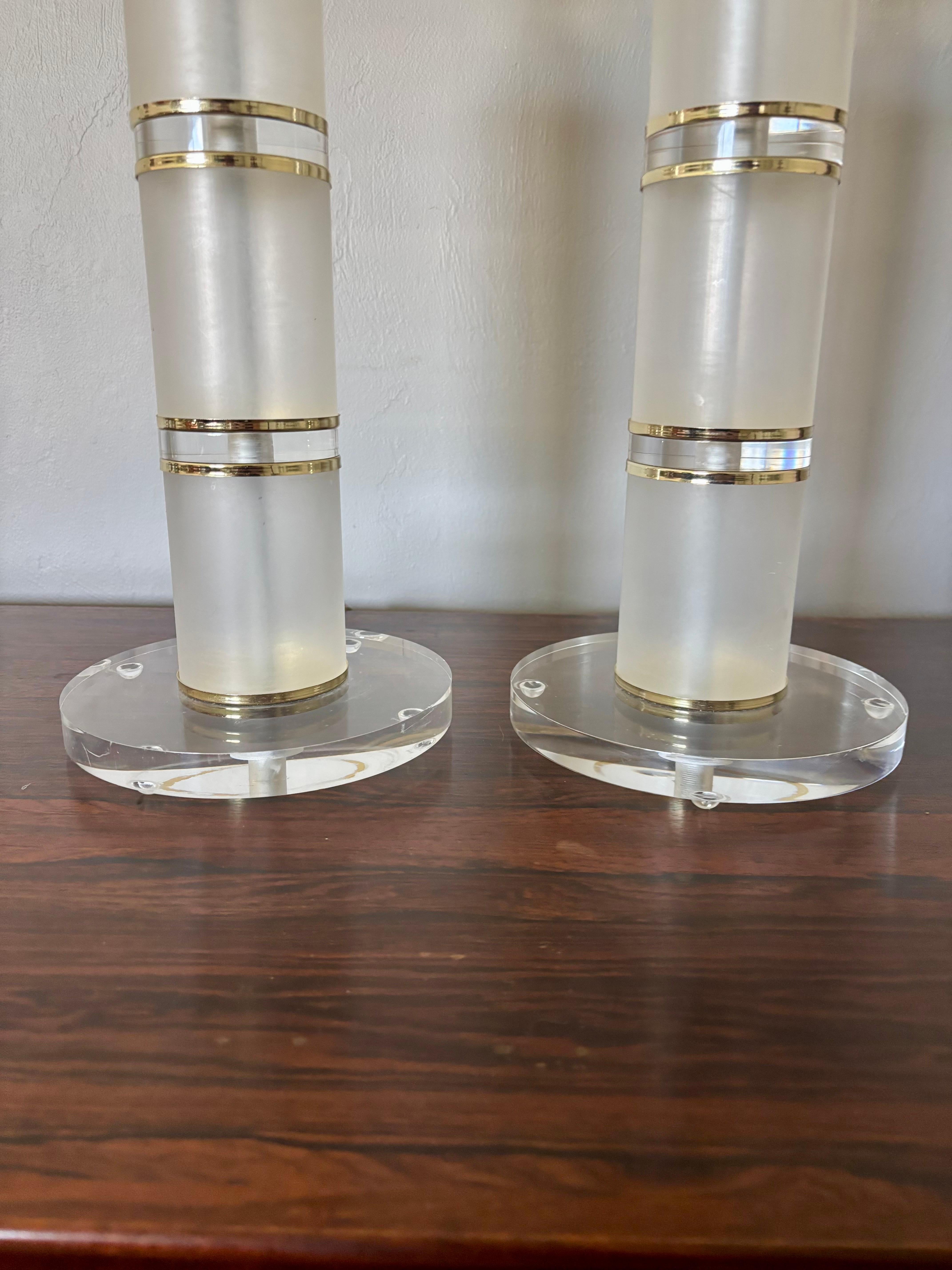 Paire de lampes de table cylindriques en lucite empilées. Composé d'une alternance de pièces en lucite givrée et claire avec des entretoises en laiton. Tige en laiton poli partant du haut et allant jusqu'à la fixation de l'ampoule. 

Fabrication
