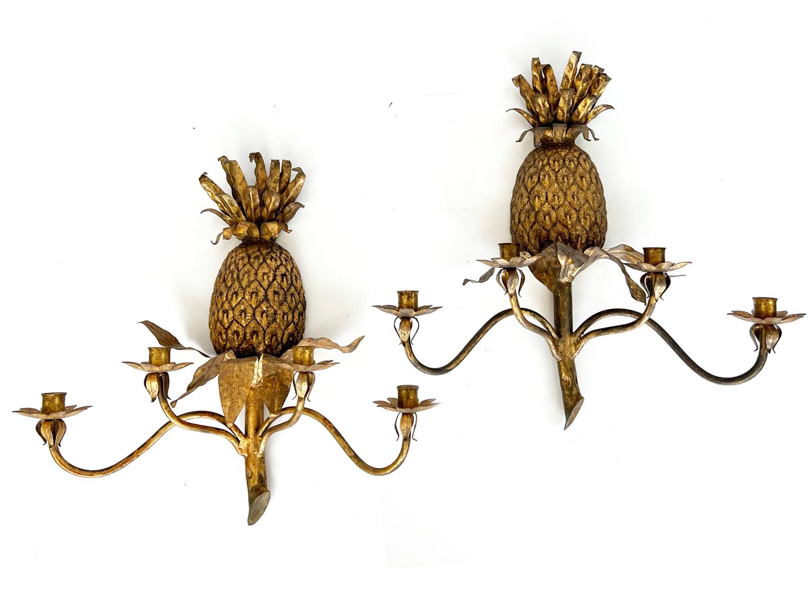 Pair of pineapple wall sconces, having a gilded finish. Each sconce has a well-articulated pineapple backplate of cast iron, surmounted with a leafy crown of tole. Four S-scroll candlearms are affixed to the stem, ending in foliate bobaches. Can be