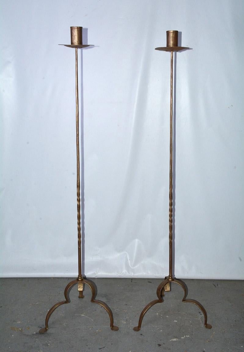 Rustic and elegant, each of the pair of vintage gilt handcrafted wrought iron candlesticks, candleholders, floor torchières, candle stands or standards has three curved legs, partially twisted decorative shafts and bobeches. The candle sockets have