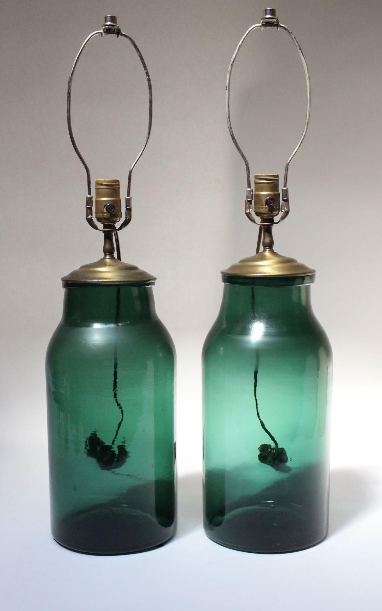 Assembled table lamps made of 19th Century blown-glass vessels in green hue with blue undertones which have been converted to lamps with the addition of brass caps/sockets (made ca. 1930s, USA).
Lamps exhibit trapped air bubbles within the glass