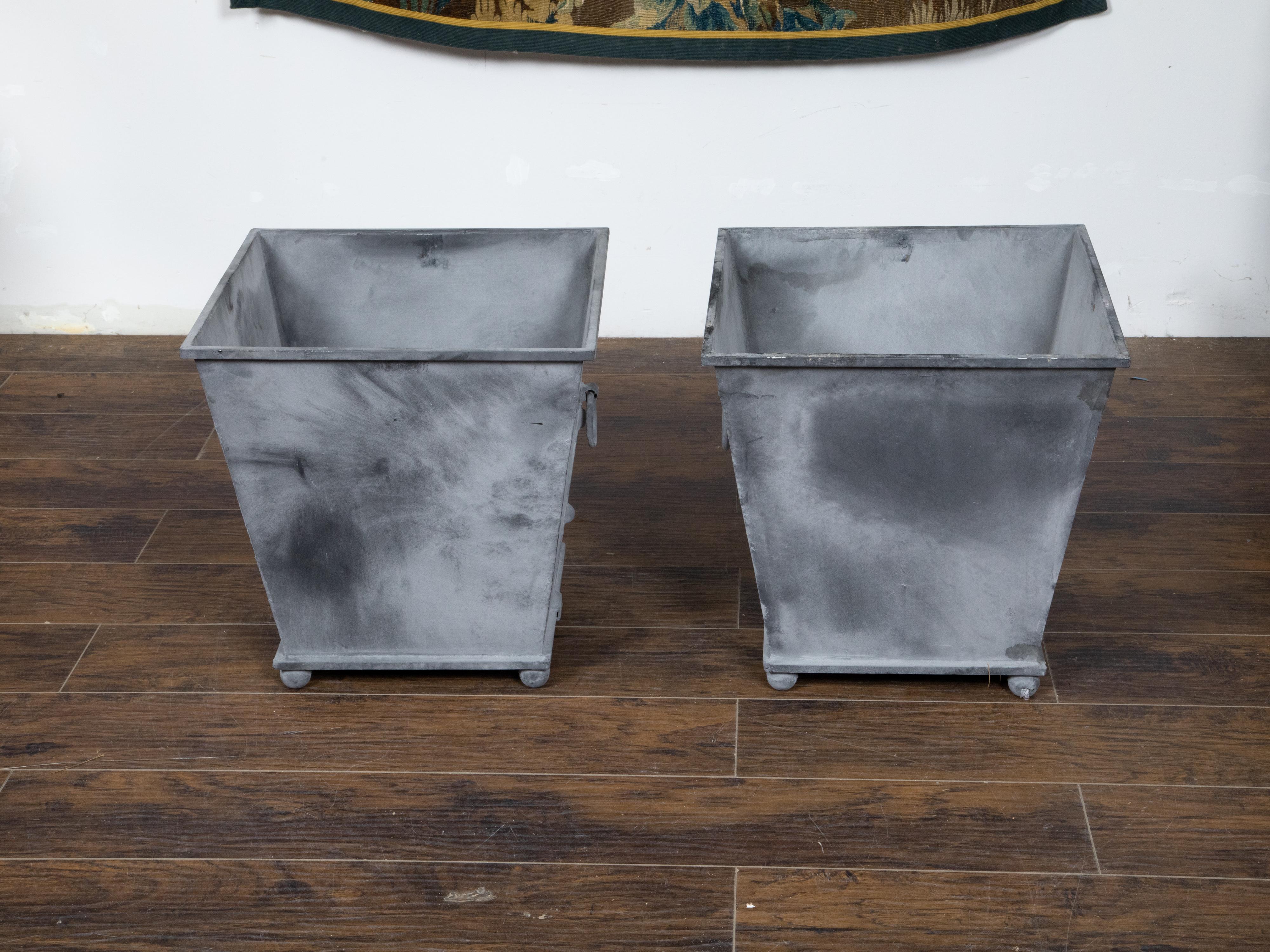 A pair of vintage metal cache pot planters from the 20th century with tapered lines, grey patinated color, lateral ring pulls and petite ball feet. Created during the 20th century, each of this pair of metal planters attracts the attention with its