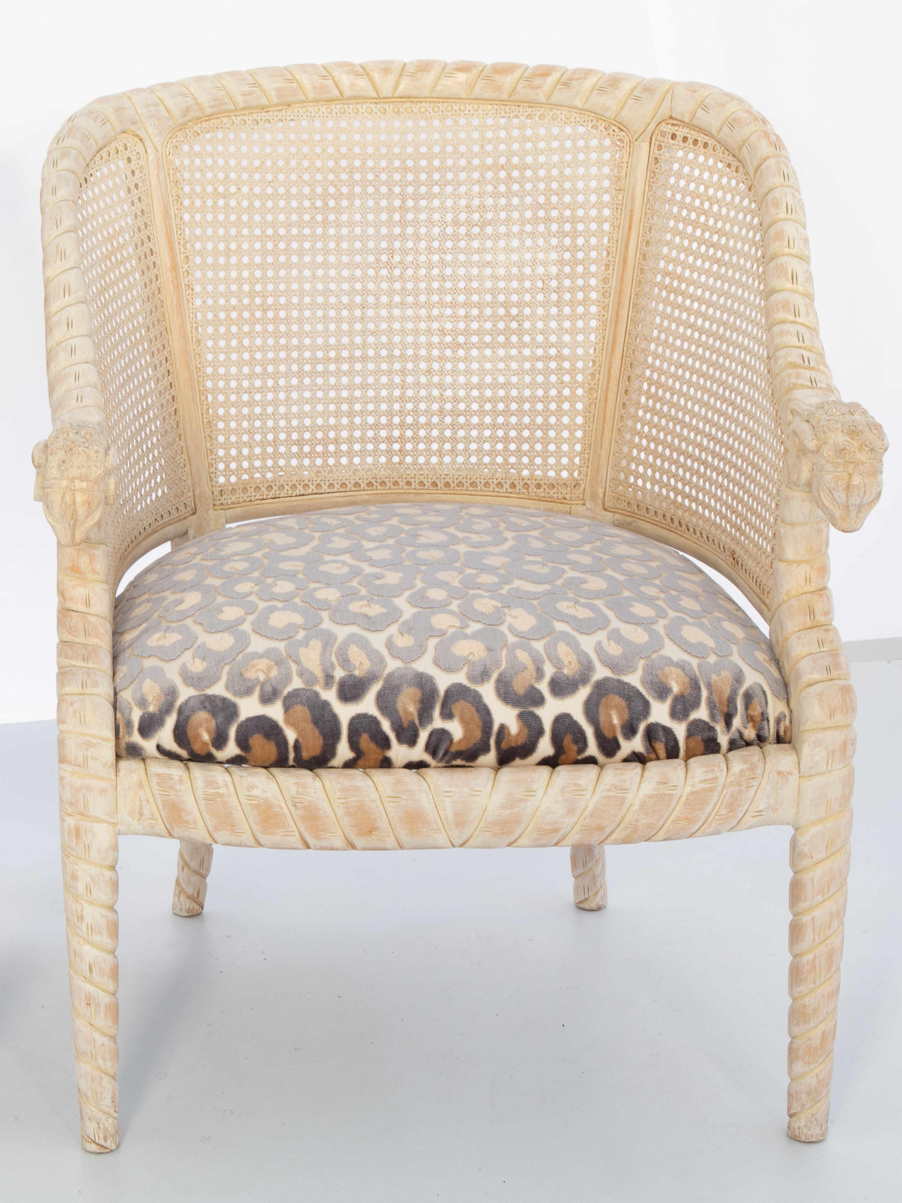 Pair of barrel-form armchairs with rope-carved frame, having pickled wood finish, upholstered in leopard chenille fabric with nailheads. Each bowed crestrail curving into arms ending in hand-carved ram's masks, over downswept terminals. Caned