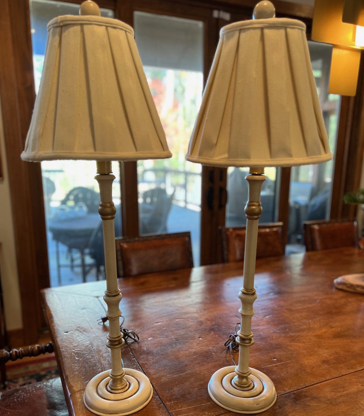 Circa 1980's, a pair of candlestick table lamps with cream pleated raw silk shades.

This stylish pair of table lamps features a classic, timeless design, perfect for adding a touch of sophistication to any traditional or vintage-inspired décor. The