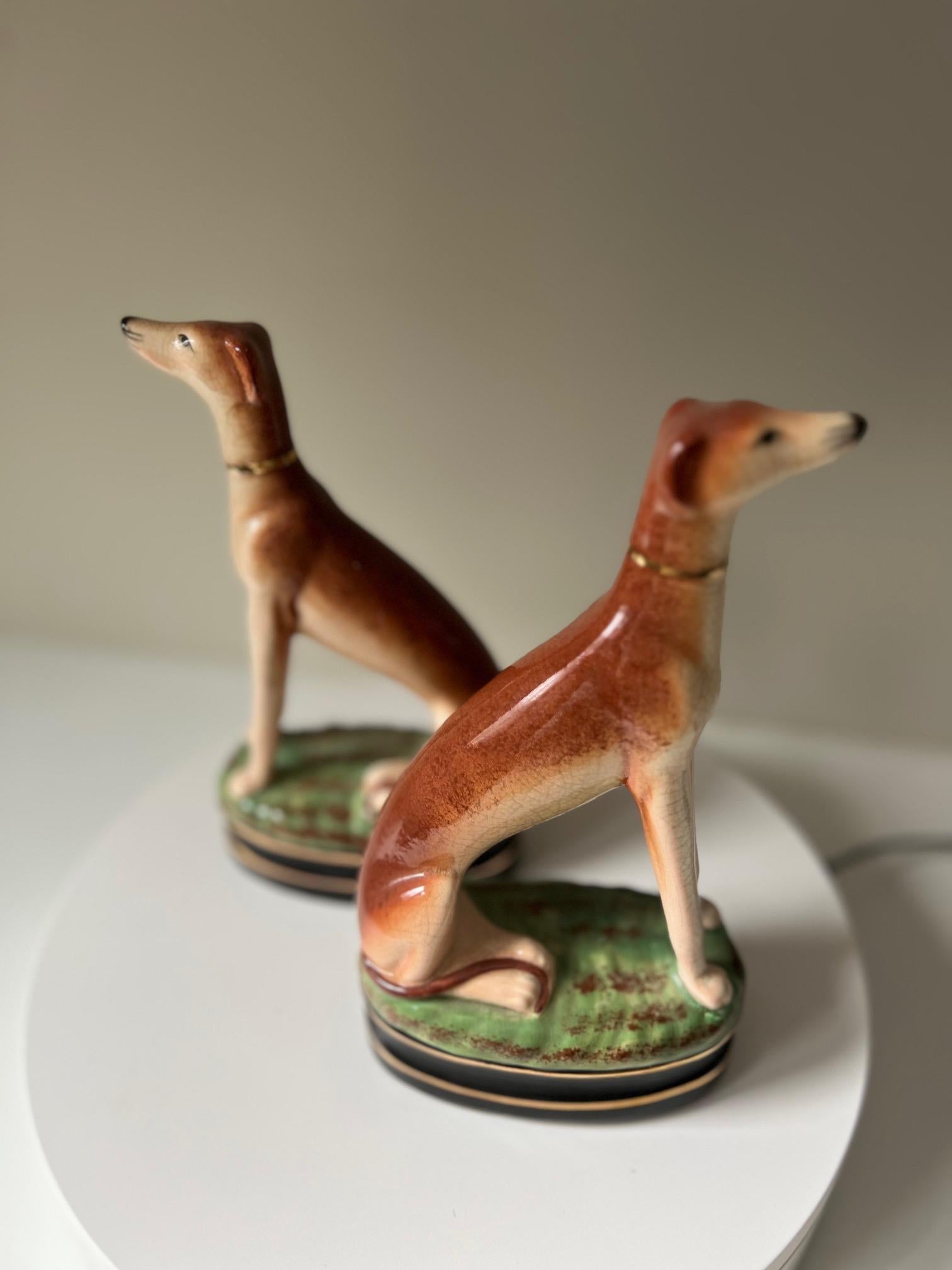 Paire de figurines de chiens Whippet de Fitz et Floyd, magnifiquement réalisées en céramique avec une finition de glaçure craquelée. Les figurines représentent deux whippets assis royalement sur des bases vertes et herbeuses avec des garnitures