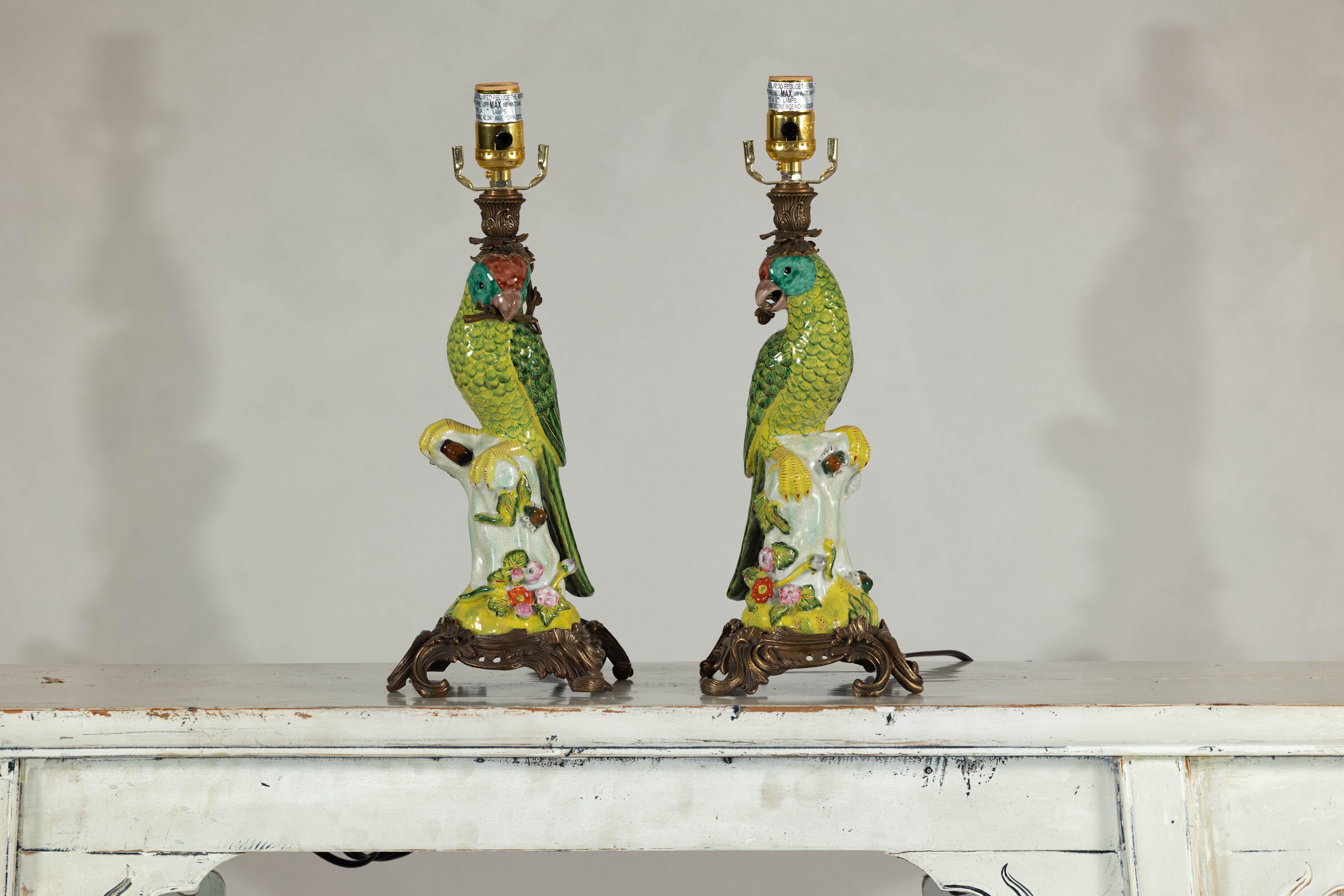 This striking pair of vintage parrot lamps captures attention with their hand-painted ceramic bodies perched on ornate brass bases. Vibrant green plumage is accented with subtle hints of turquoise and deep red, lending a lifelike quality to each
