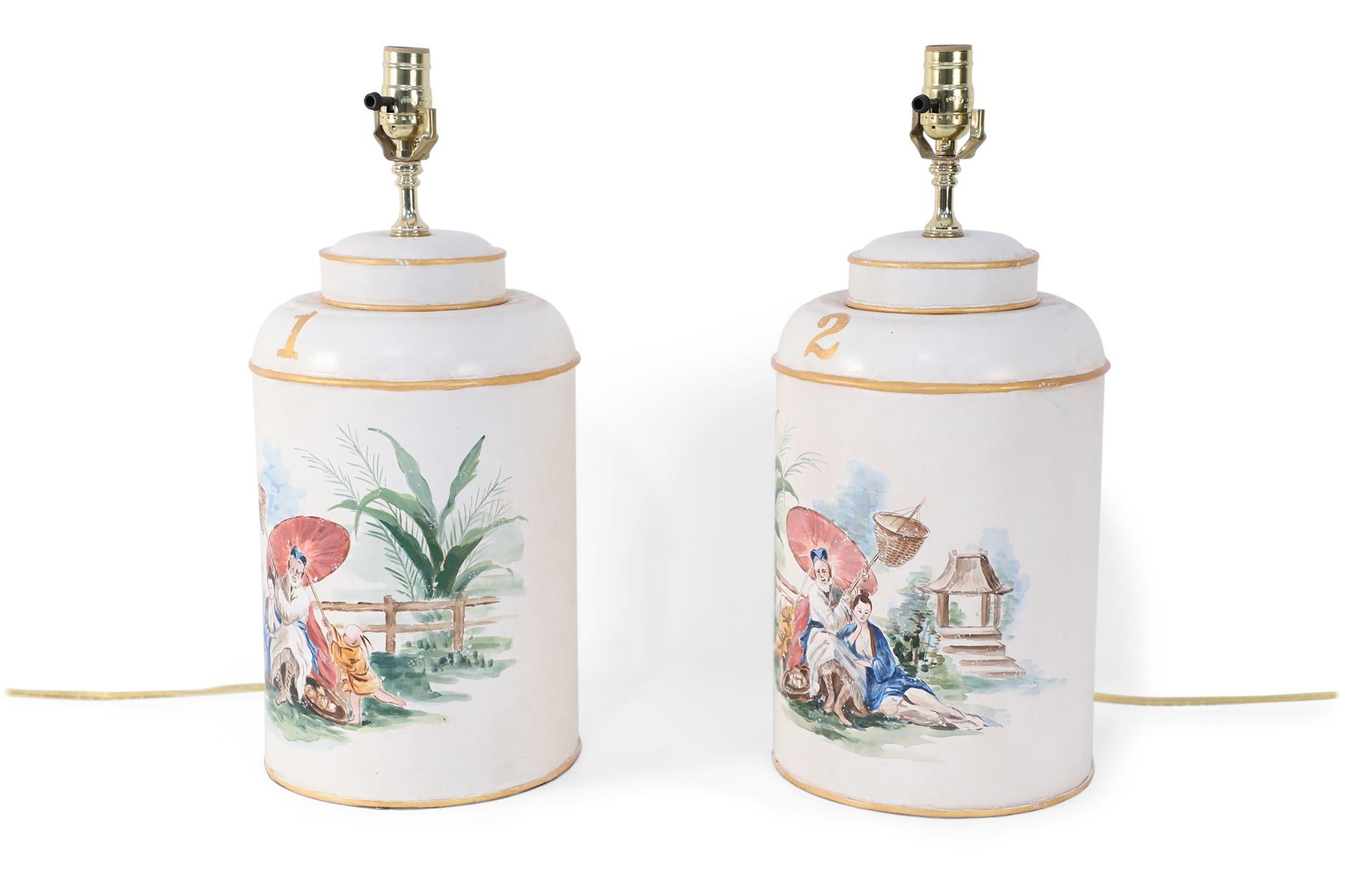 Pair of Chinese vintage tole table lamps with a hand painted outdoor scene of a figure sitting under a parasol in a garden against an off-white background with gold painted numbers.