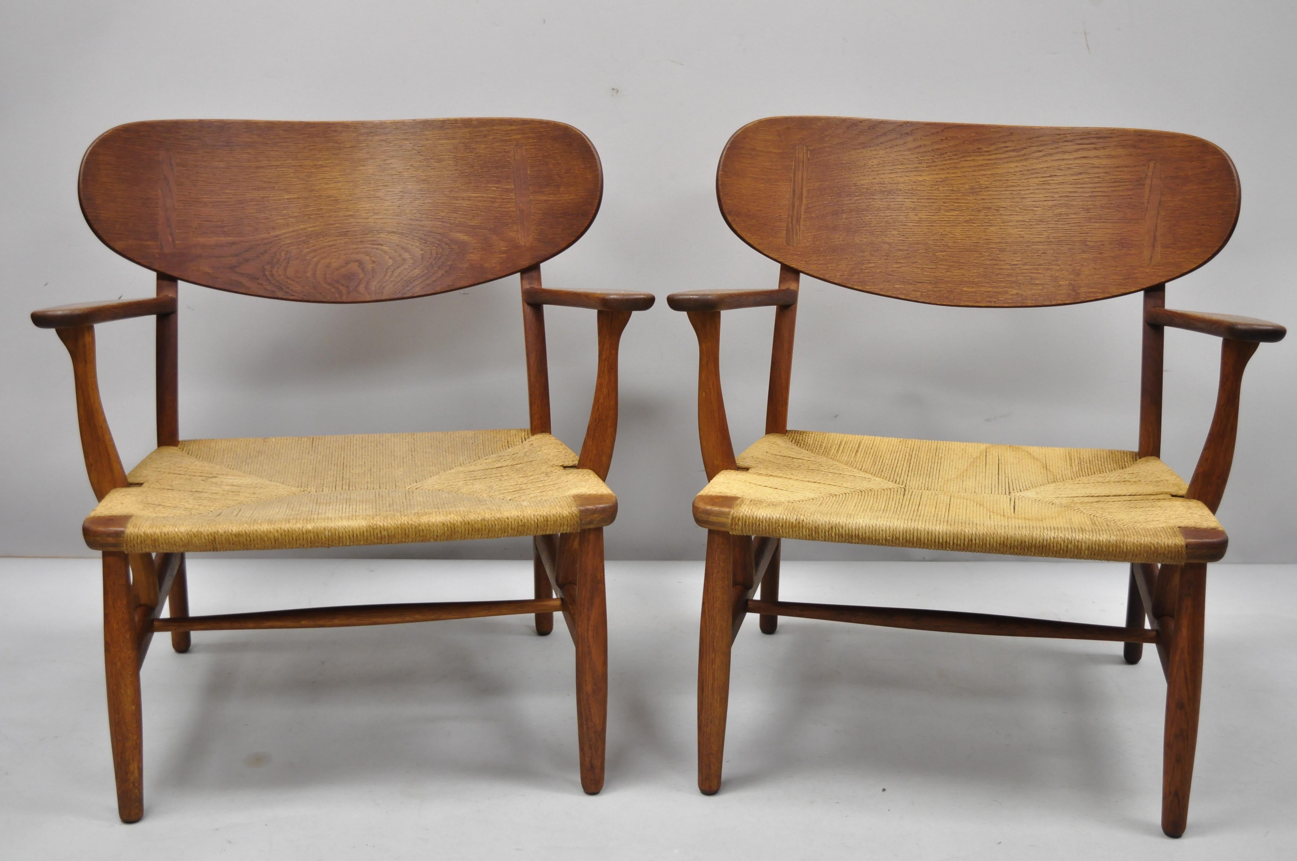 Pair of vintage Hans Wegner CH22 Carl Hansen & Son oak lounge chairs. Item features woven paper cord, solid oakwood frames, beautiful wood grain, original Hans Wegner stamps to underside, quality Danish craftsmanship, great style. Measurements: