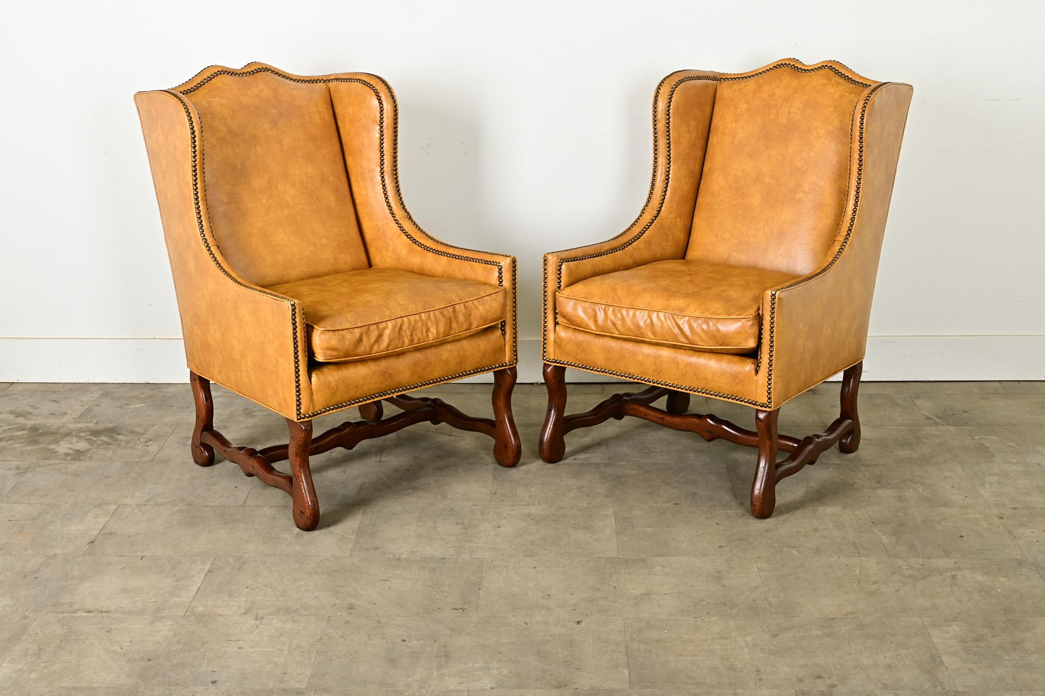 A wonderful pair of 20th century Os de Mouton style wingback chairs, by American firm Henredon, who specialized in American-made furniture with European silhouettes. These large armchairs are upholstered in a buttery faux leather and trimmed in