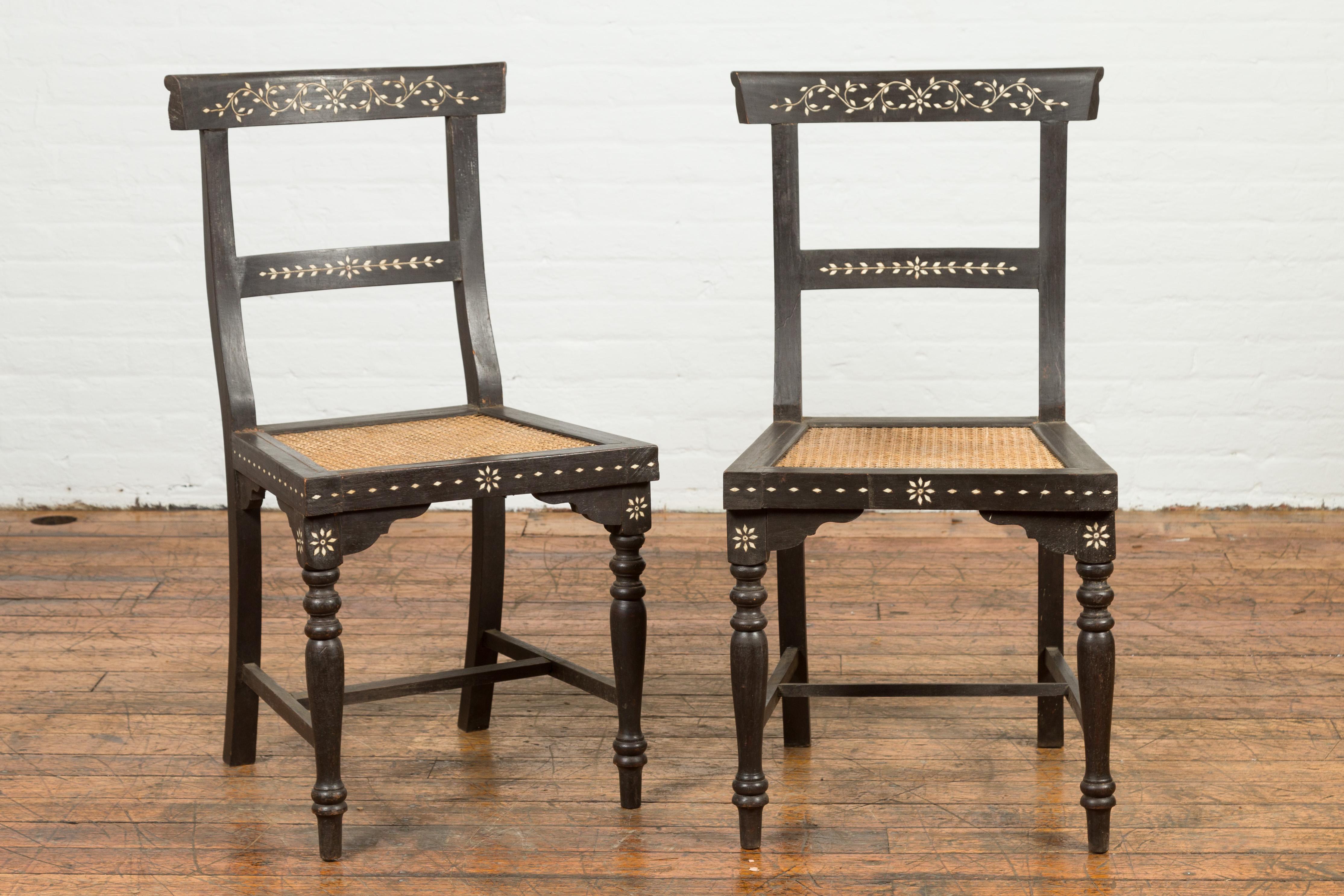 A pair of Indian vintage black stained side chairs from the mid-20th century, with mother of pearl inlay and rattan seat. Created in India during the midcentury period, each of this pair of side chairs charms us with its curving back, adorned with