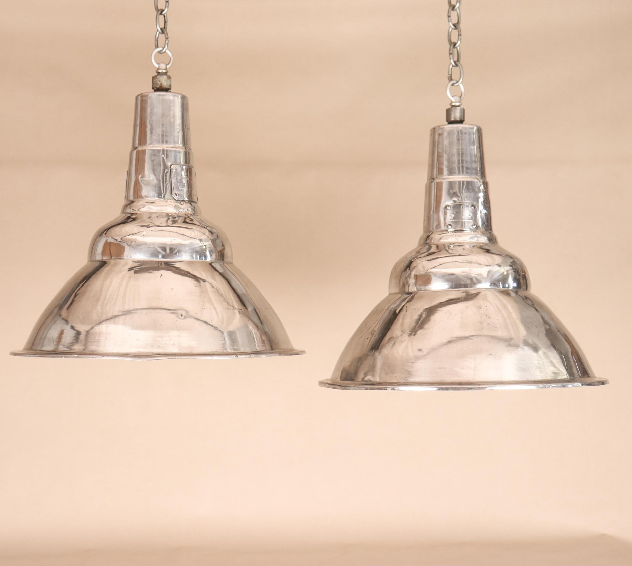 A pair of clean, simple polished aluminum Industrial pendant lights, circa 1960. These vintage floodlights have been newly re-wired with porcelain sockets and disseminate a wide beam, making them ideal over a kitchen island, a game table, or in a