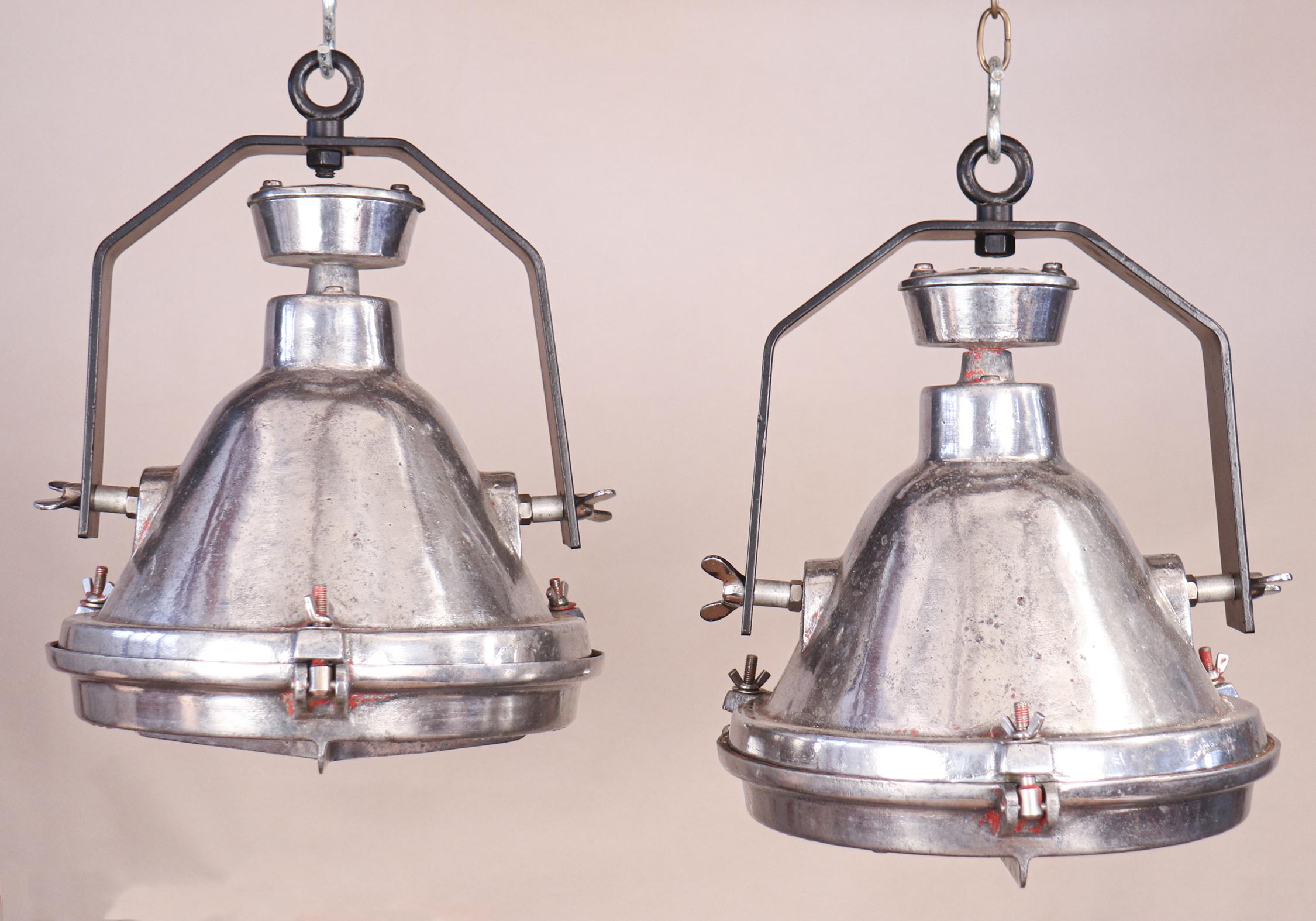 A cool pair of salvaged and restored cast aluminum Industrial pendants with iron brackets, circa 1960. These midcentury ship's cargo lights have clean form and are versatilely sized. Minor traces of red paint add character to the pendants (see