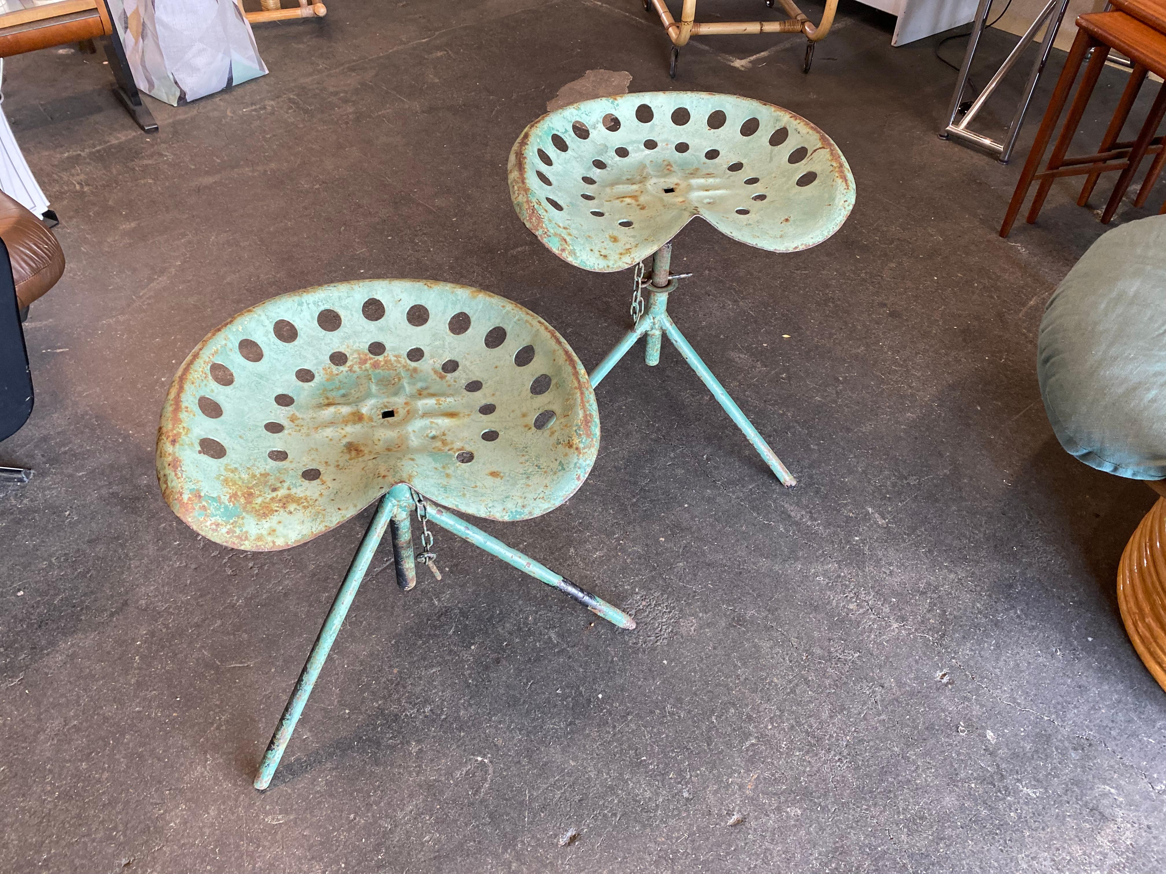 Pair of rare industrial style tractor seat stools. The stools have a gorgeous green color and patina. You can find a variety of replica seats of this type. Both of these are really from the 1920's. The iron seats have been repainted many times,