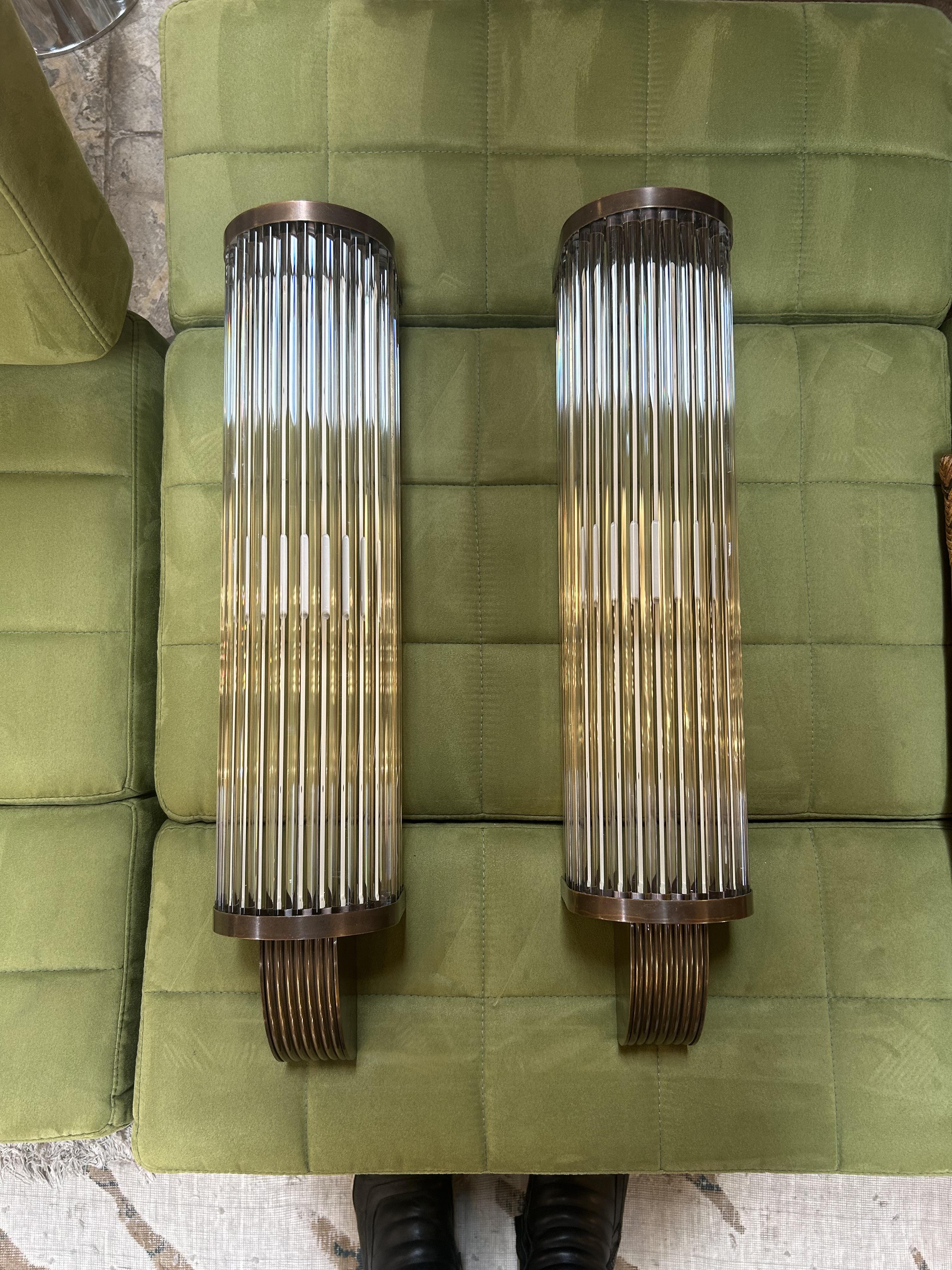 This pair of vintage Italian wall sconces captures the essence of Art Deco glamour, evoking the opulence of The Great Gatsby era. Each sconce features a cascade of vertically aligned glass rods encased in a bronze-patinated frame, casting a warm,