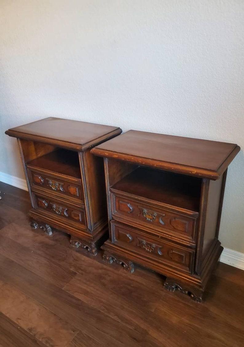 A handsome pair of Italian bedside chests, born in the mid 20th century, in a distressed rustic finish, fitted with one open shelf, over two drawers, having hanging scrolled pulls, rising on molded base, over carved scrolling feet. Circa 1940s,