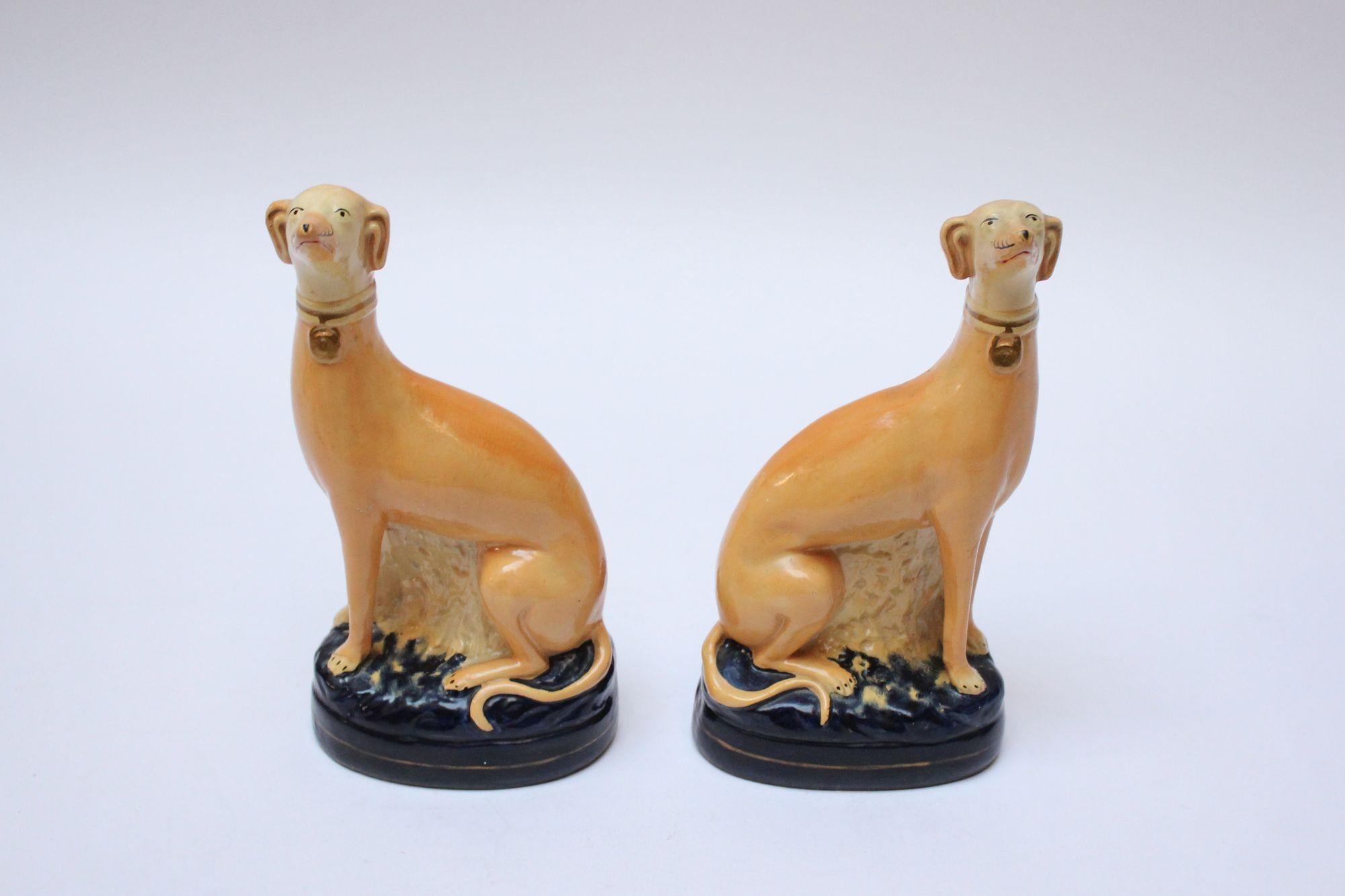 Pair of Staffordshire-style porcelain Italian greyhound/whippet bookends by Borghese (Italy, ca. late 1920s/early 1930s). Composed of statuesque, tan greyhounds with black hand-painted facial/paw details and gold collars perched on navy-blue poufs.