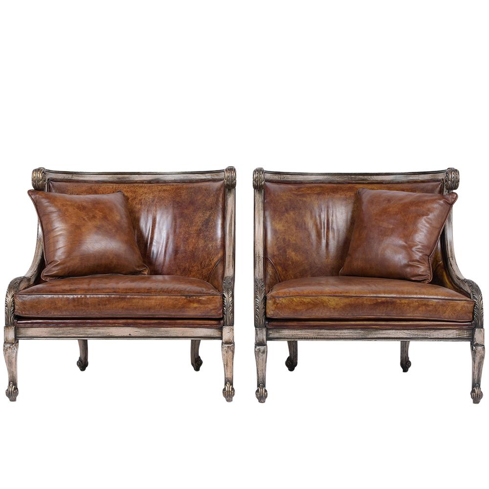 This pair of leather carved armchairs has been restored and is in great condition. These chairs have a carved scroll arms design, curved backs, have been painted in an off-color with gilt details and have a distressed finish. The chairs are
