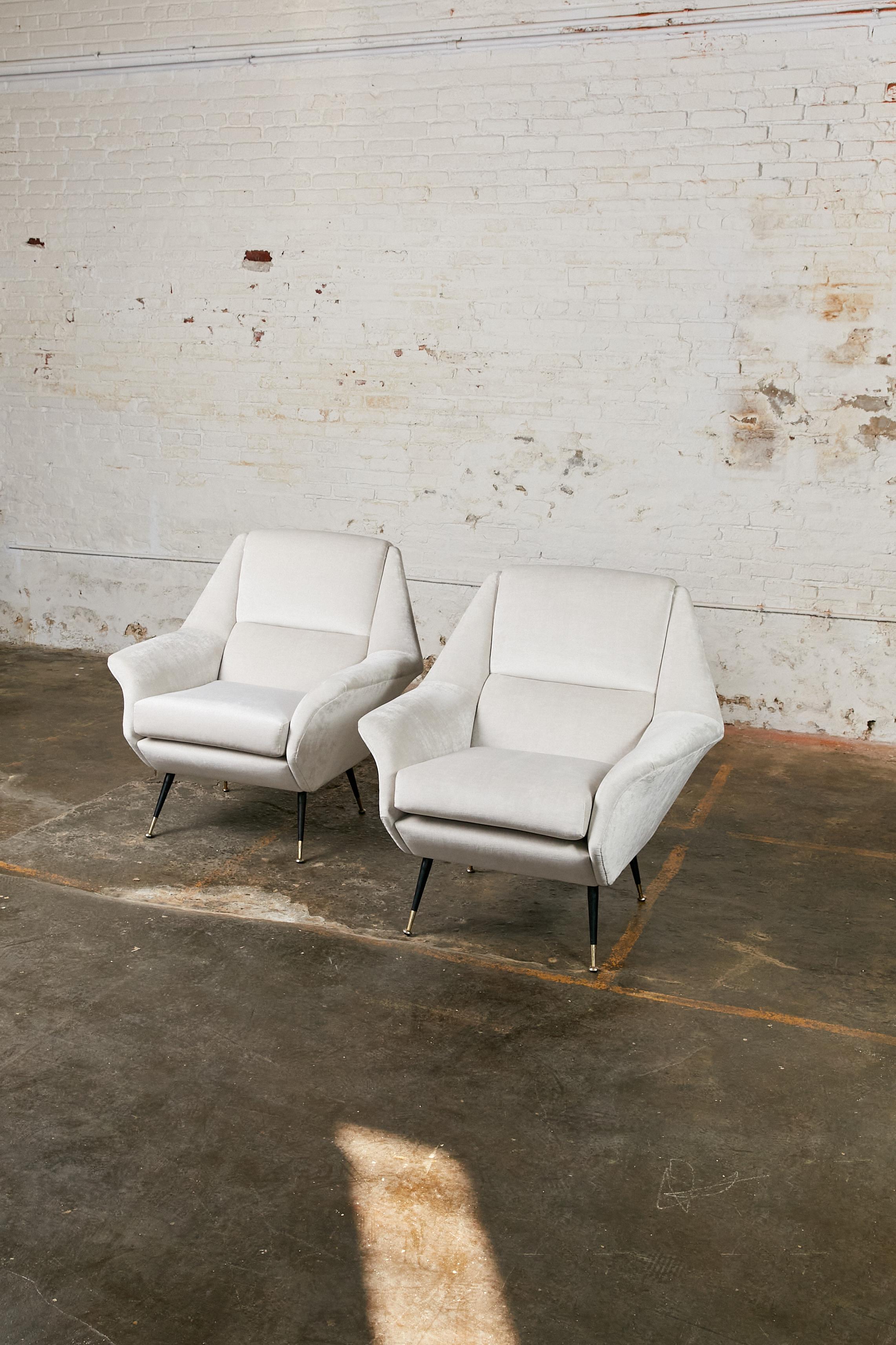 Set of two Italian Mid-Century Modern lounge chairs. They feature a tapered, gently reclined back with a rounded top. The chairs sit on metal feet that finish in rounded concave stands. Fully re-upholstered in light grey velvet.