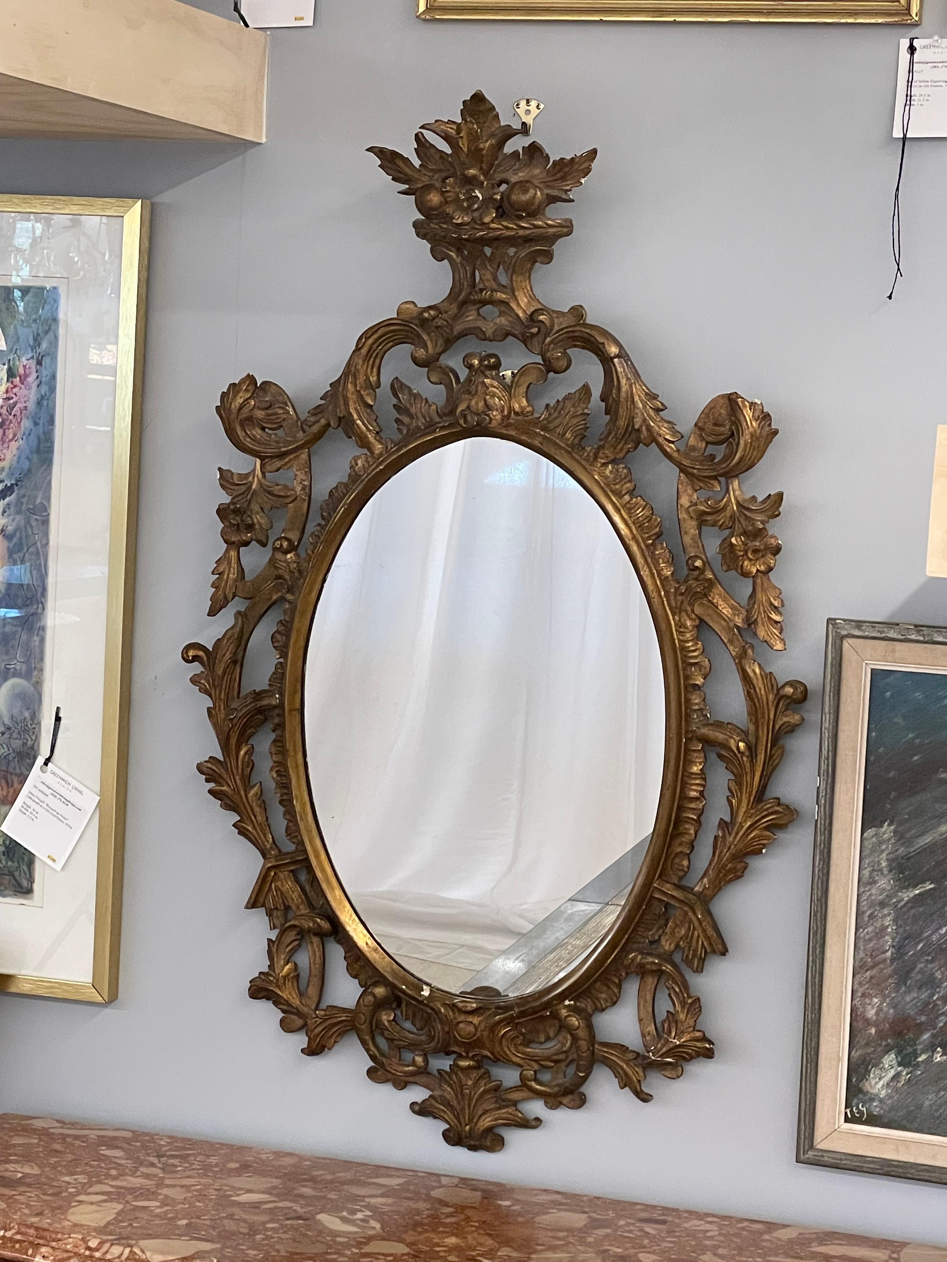 A pair of Italian wall or console mirrors. Each having pierced floral carvings terminating in a basket of flowers and fruit. The gilt gold frame flanking an oval shaped mirror.