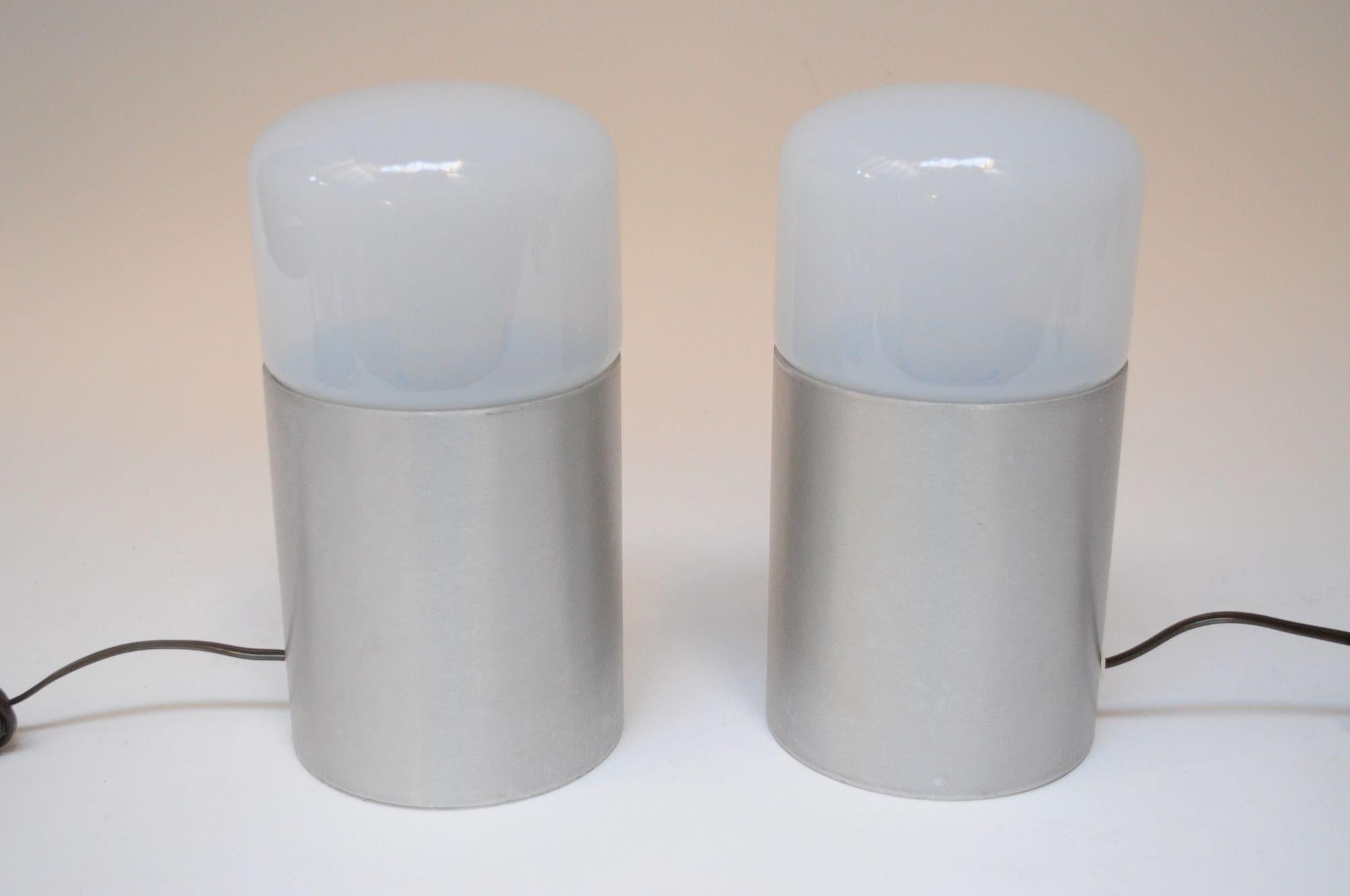 Pair of sleek, modernist bedside/tables lamps sourced from a hotel in Chianciano, Tuscany (ca. 1960s, Italy).
Composed of brushed aluminum cylindrical bases supporting blown opaline/milk glass shades.
Very good, vintage condition with minor wear to