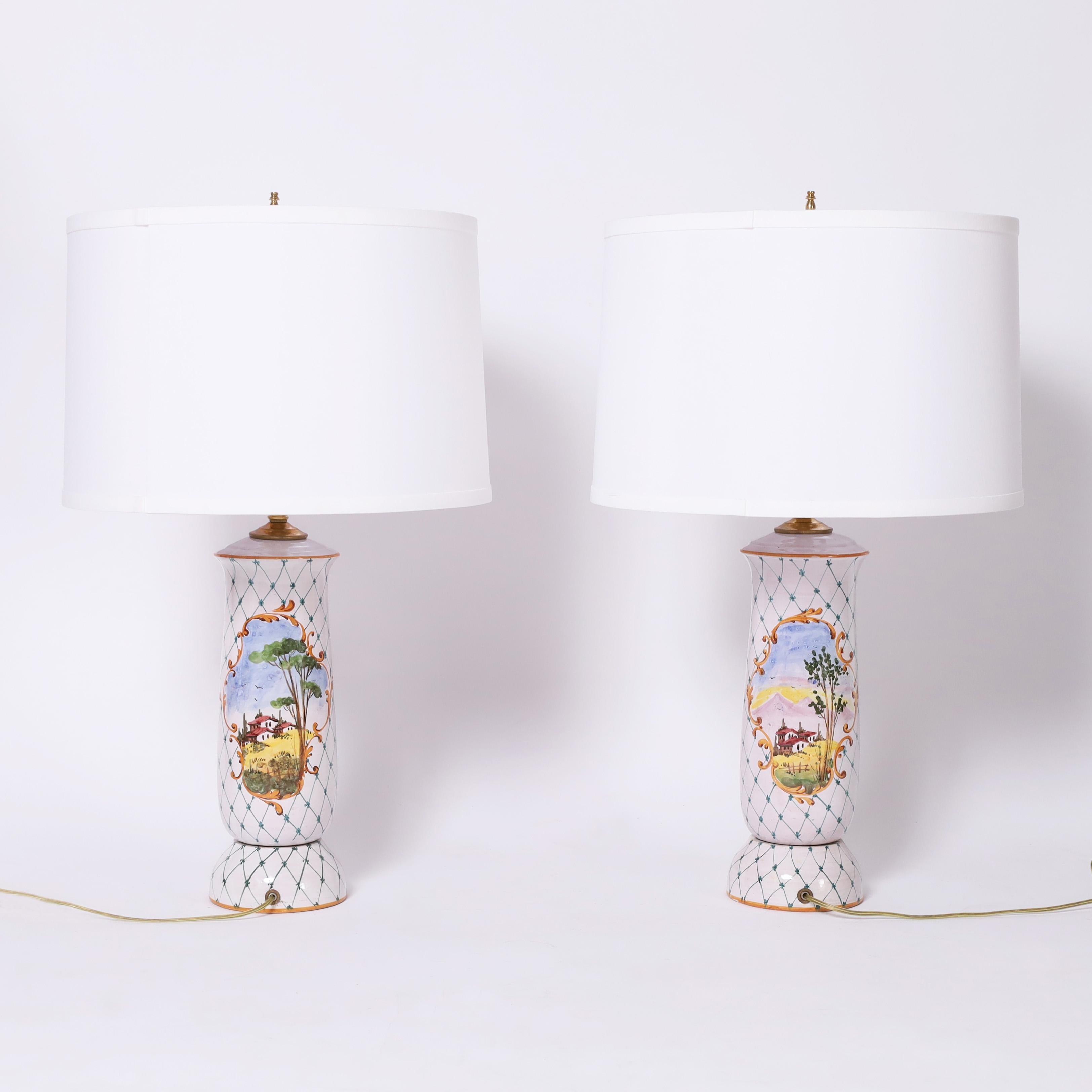 Coppia di lampade da tavolo italiane della metà del secolo scorso realizzate in terracotta con paesaggi decorati a mano in una finestra a cartiglio su sfondo bianco con traliccio. 