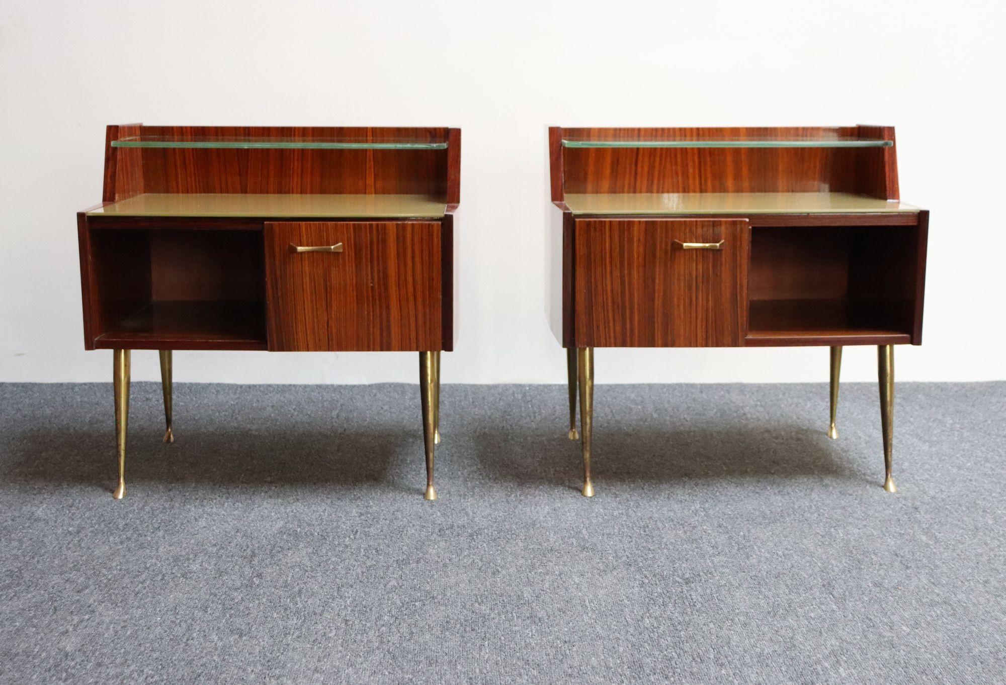 Pair of rosewood nightstands/bedside tables with dual storage cubbies (single door concealing one section; the other is open by design) and brass pulls along with sculptural brass legs (ca. 1950s, Italy). Ample surface spaces with split level