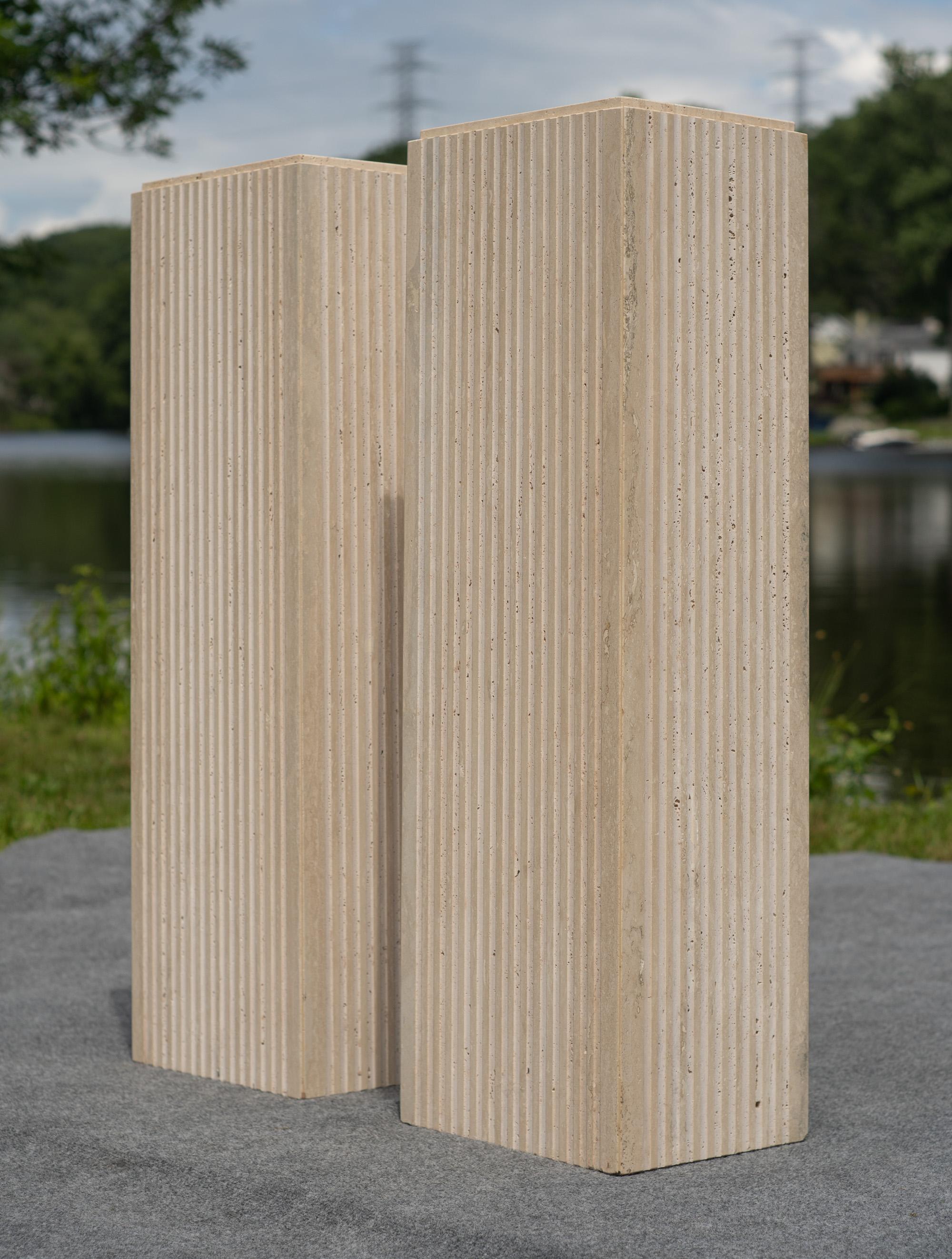 Designed in Italy after the style of legendary Italian architectural genius Angelo Mangiarotti, this pair of pedestals feature solid travertine construction, accented with a raised platform and tens of flutes carved away from the sides. These design