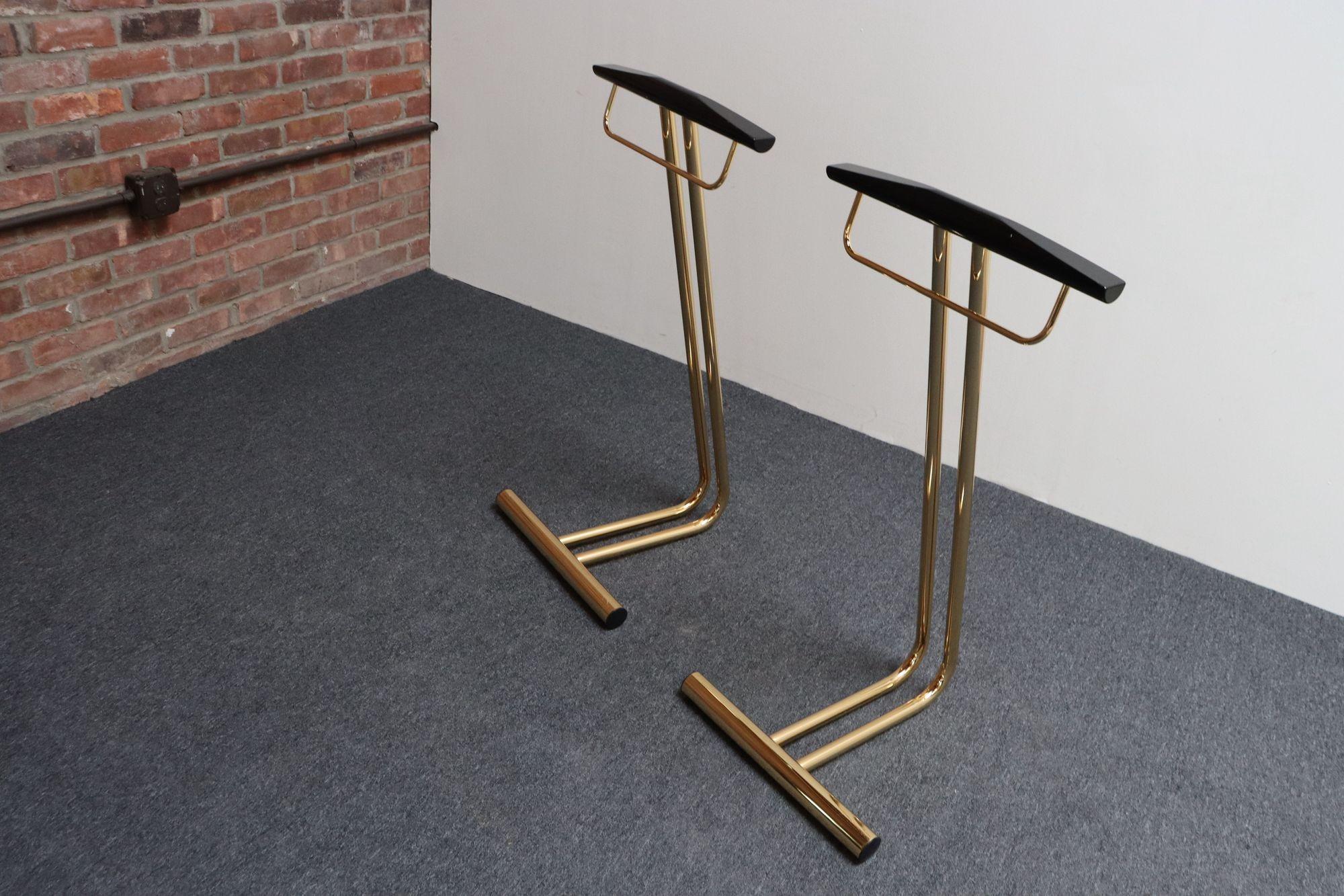 Pair of sculptural Italian valets/dress boys (ca. 1960s, Italy).
Composed of a polished tubular brass frame with black lacquered wooden hanger and brass bar for hanging scarves, ties, or pants). The base can be used for storing shoes.
Black lacquer