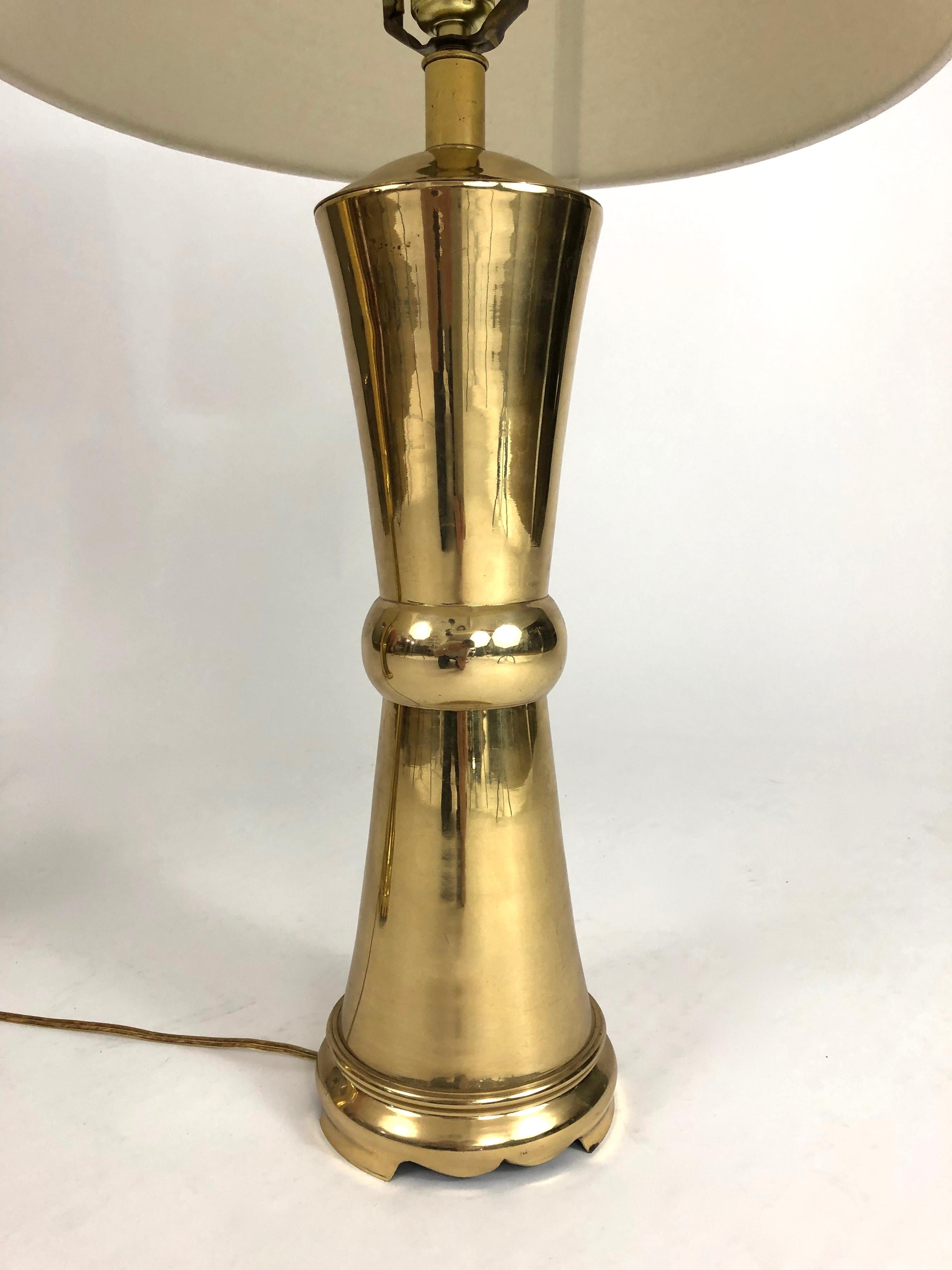 A pair of high quality, vintage solid brass lamps in the manner of James Mont and made by Frederick Cooper, Chicago. The form is inspired by an ancient Asian metal form, cylindrical with tapering top and bottom and a band around the middle, raised
