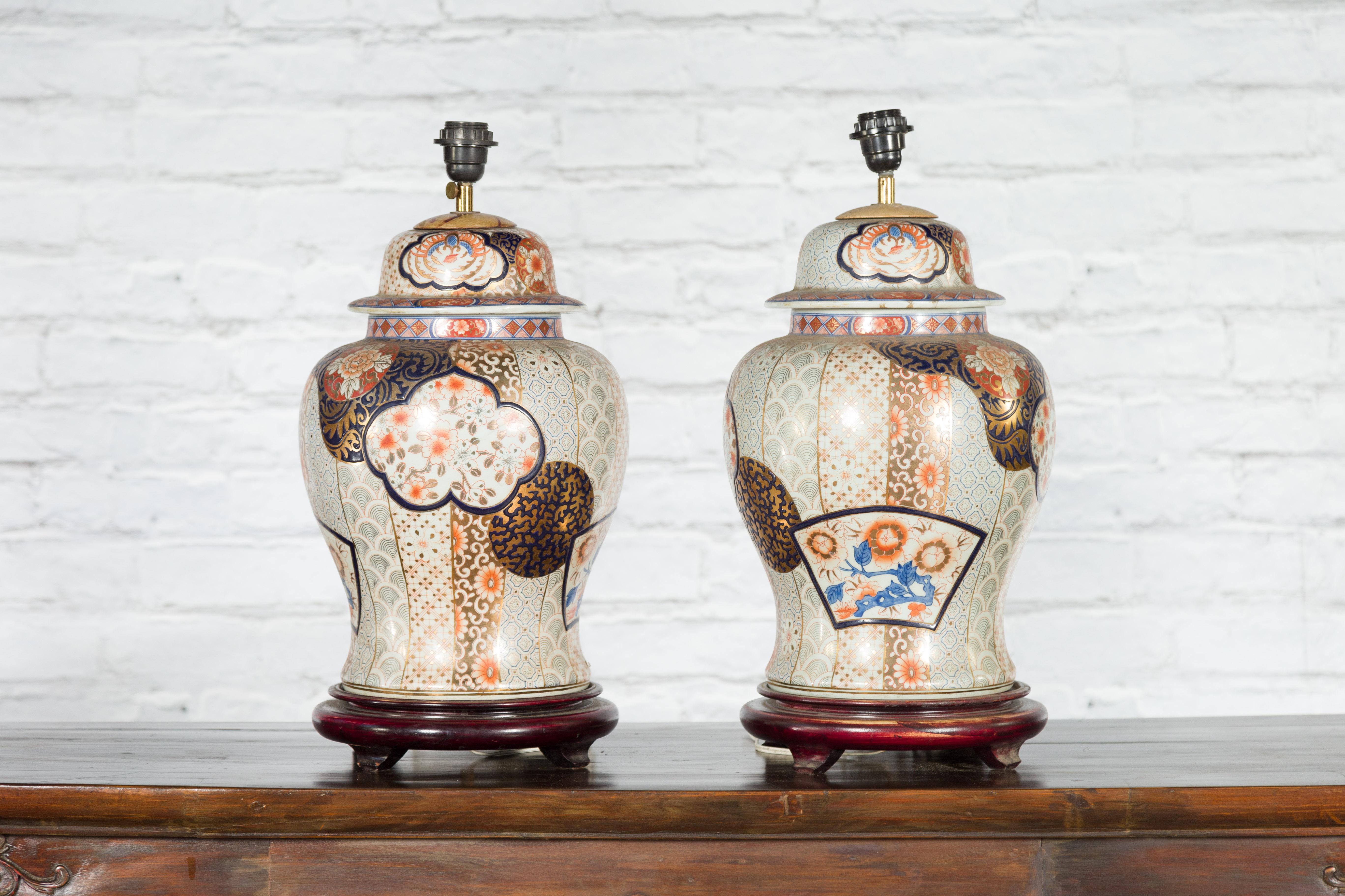 A pair of Japanese Arita porcelain table lamps from the mid-20th century, with gold, blue and orange tones, domed lids and round wooden bases. Created in Japan during the midcentury period, each of this pair of Arita ware vases, mounted as table