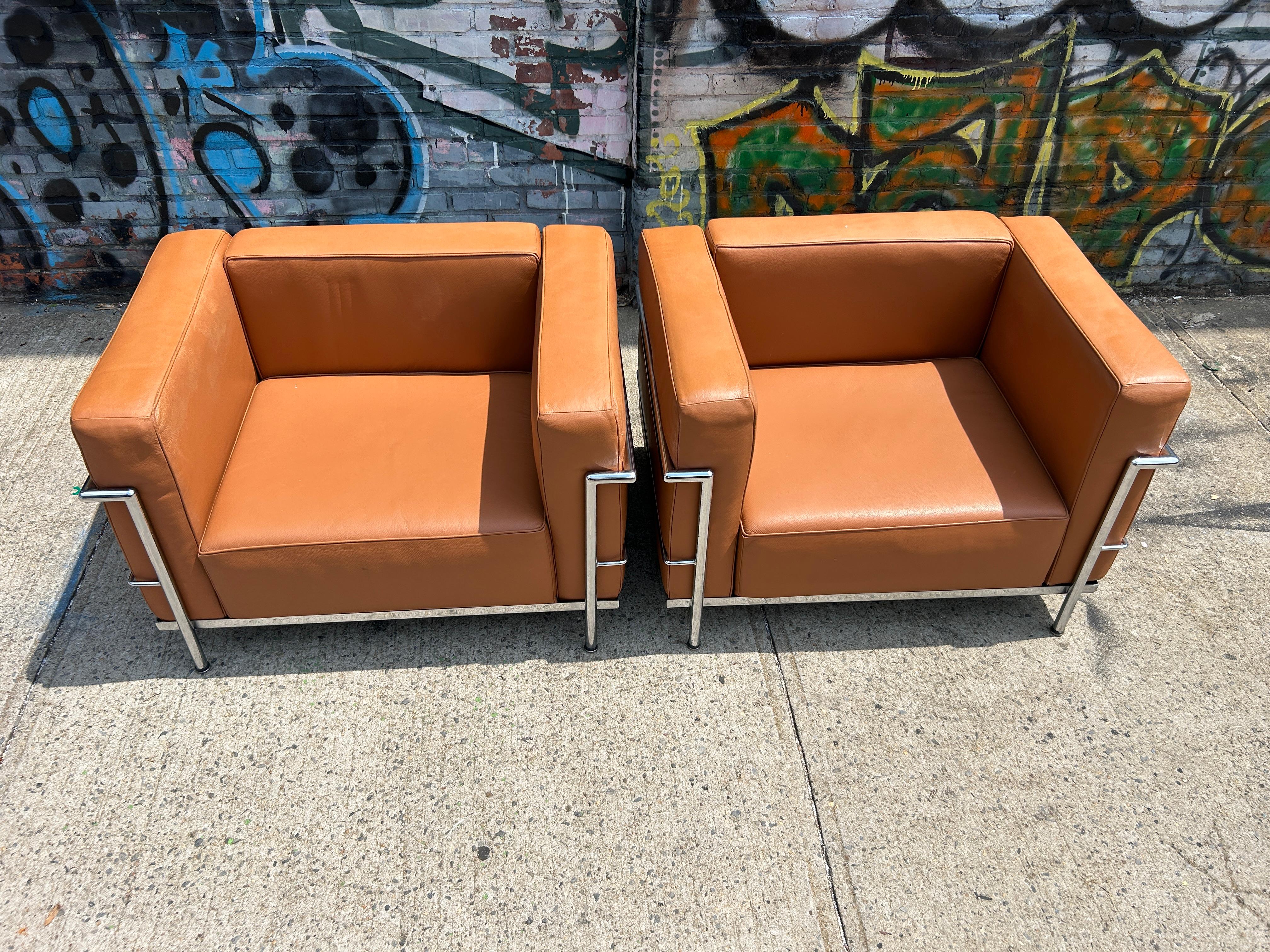 A pair of Vintage lounge or club chairs by Le Corbusier. Wide Model LC3 in Tan Leather. Triple chrome plated steel frame. Show normal signs of use on top of arms from over the years. Manufactured by Gordon International. All straps are good all