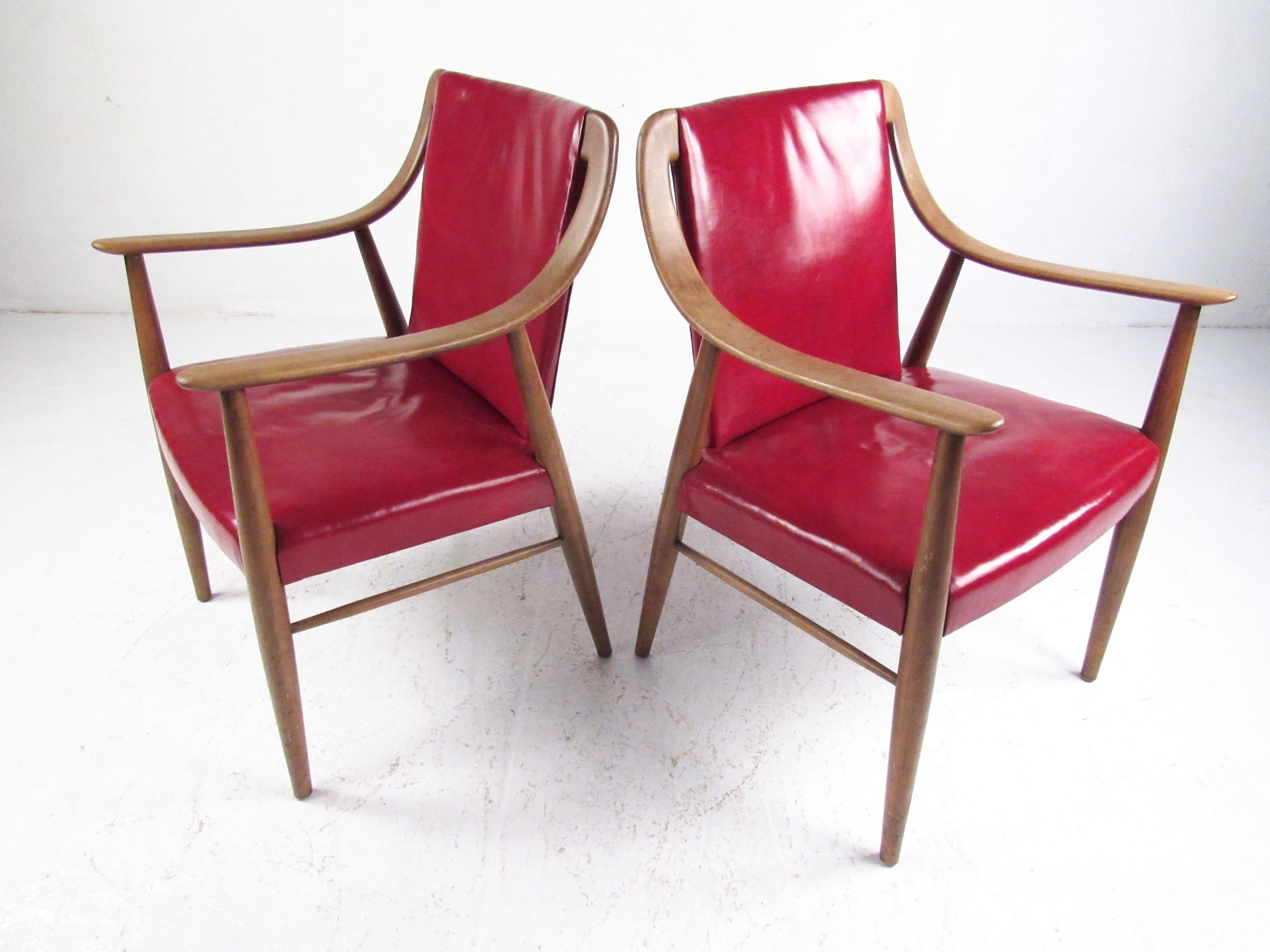 This stylish pair of Scandinavian Modern side chairs feature vintage red leather upholstery and sculpted solid wood frames. The unique Mid-Century Modern appeal of these Peter Hvidt style arm chairs make a great addition to home or office seating.