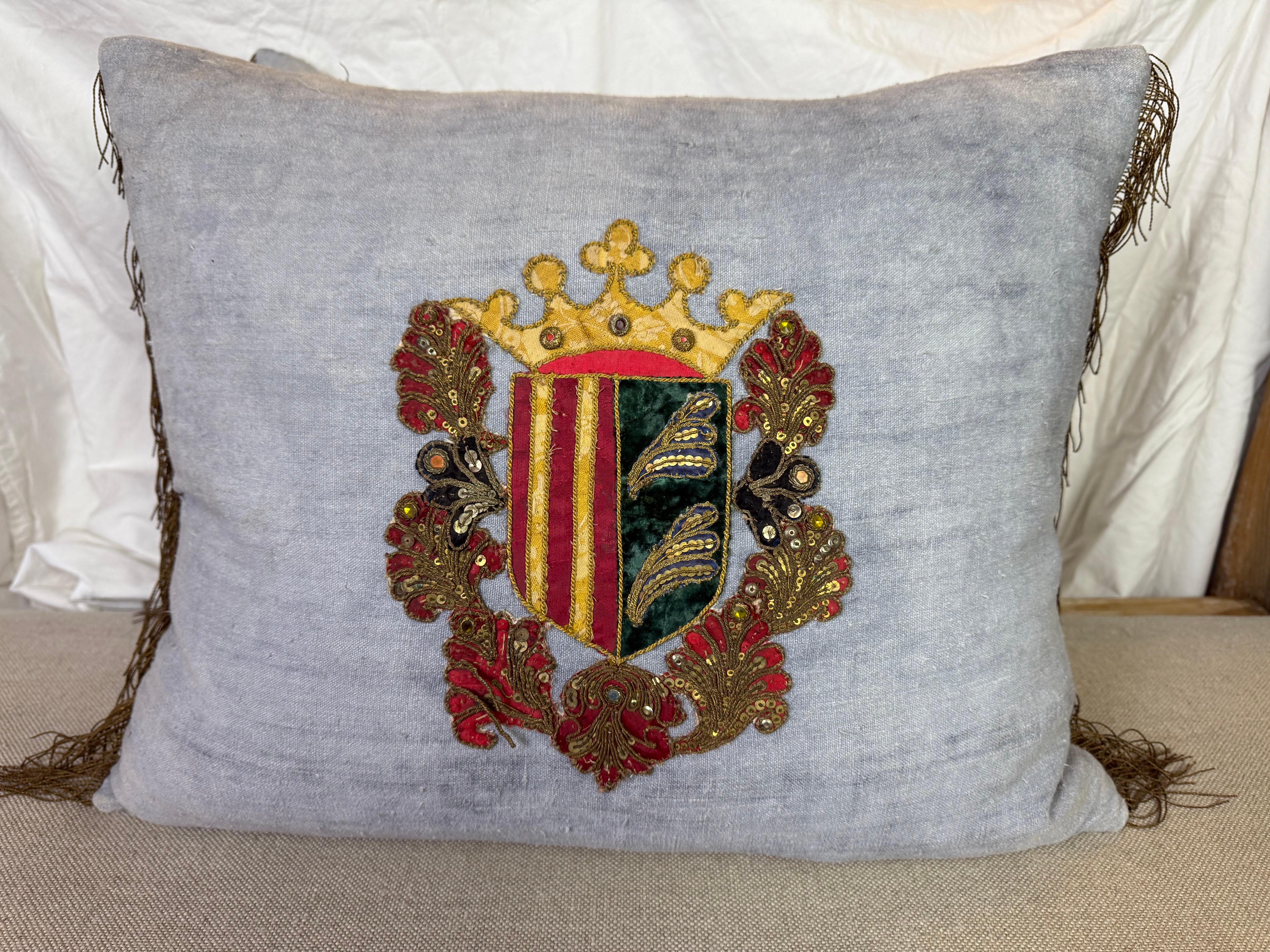 Dieses exquisite Paar Vintage-Kissen aus Leinen zeigt opulente Wappenapplikationen aus Metall und Seide aus dem 19. Jahrhundert. Jedes Kissen zeigt ein königliches Wappenmotiv, das sorgfältig mit gold- und silberfarbenen Metallfäden, Pailletten und