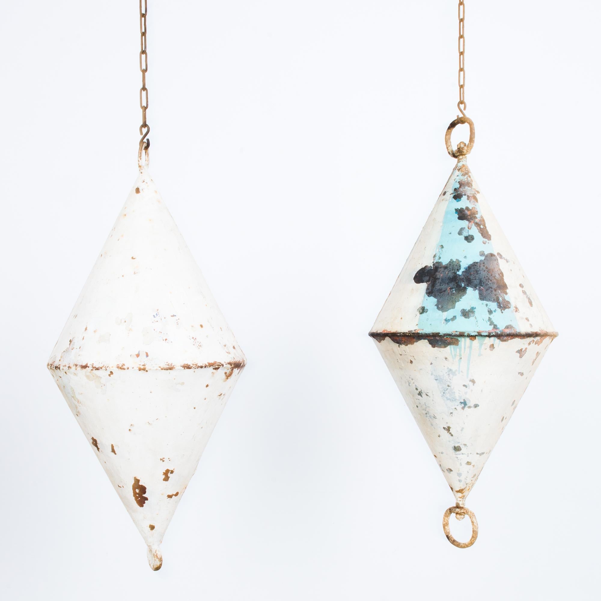 This pair of bicone-shaped metal buoys was made in Belgium, circa 1950. Both buoys hang from chains and are painted white with triangular sky blue areas on one. They sport an oxidized patina and will bring a coastal charm to your interior space.