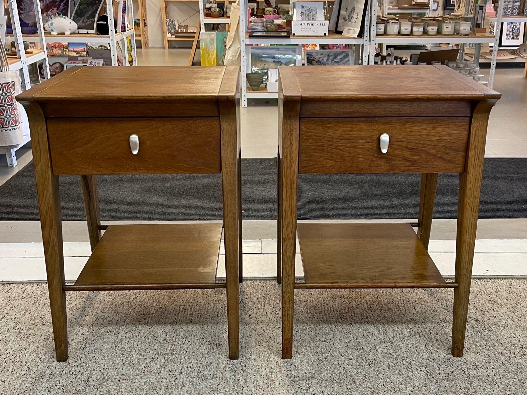 These end tables have an overhanging top with sculpted leg fronts. Lower shelf beneath a single dovetailed drawer with original hardware. Unique wood grain. Circa 1960s. Vintage Condition Consistent with Age as Pictured.

Dimensions. 18 W ; 16 D ;