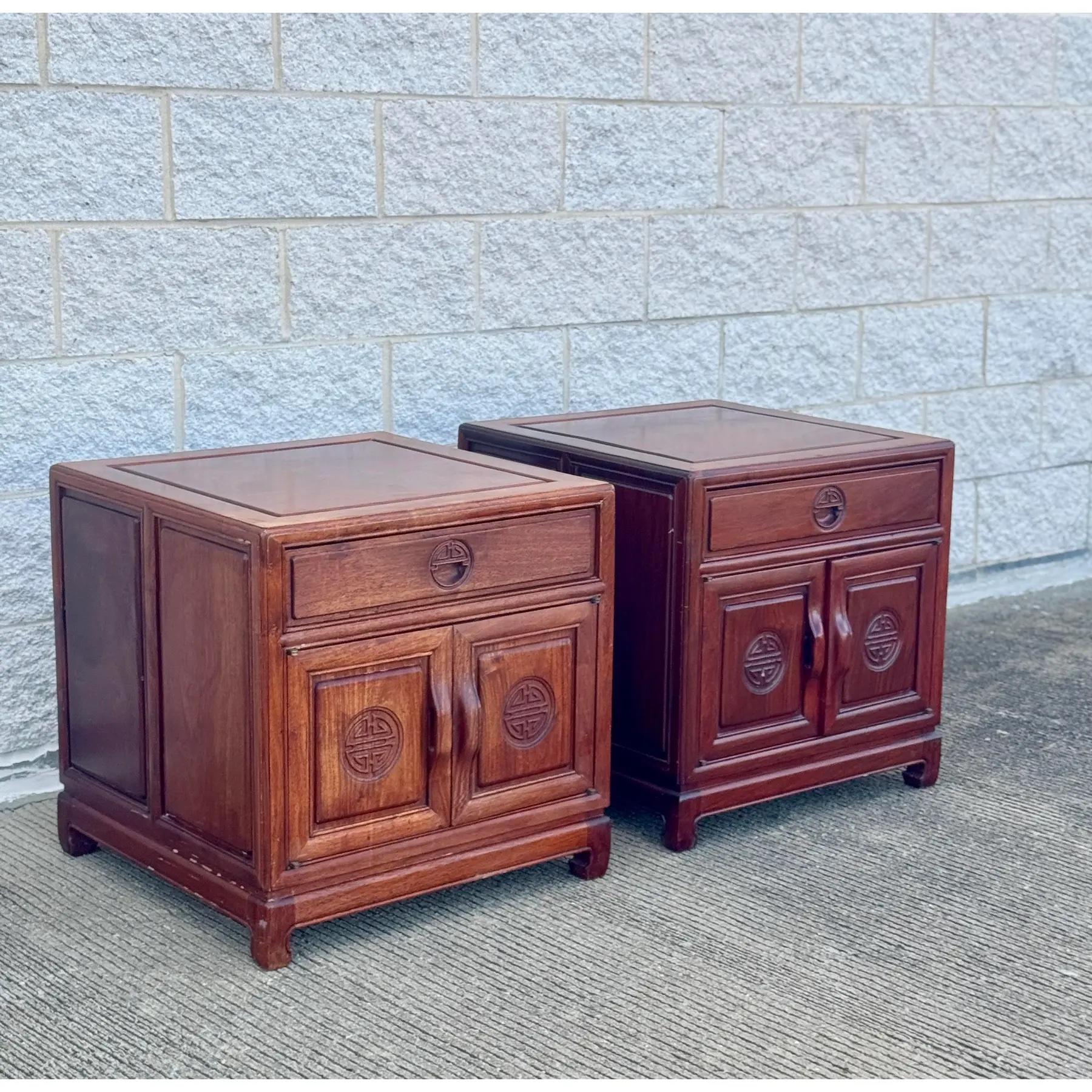 A beautifully crafted pair of vintage rosewood nightstands inspired by traditional Ming Dynasty design. Each piece features a single drawer over double doors, adorned with circular longevity medallions and classic recessed paneling. The rich