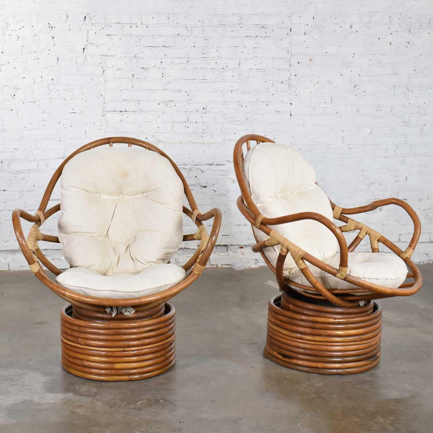 Handsome and fun pair of modern rattan swivel, Mamasan, bucket shaped lounge chairs with a white set of cushions. The chairs are in fabulous vintage condition. All the rattan needed was a good cleaning. The cushions have some stains so most likely