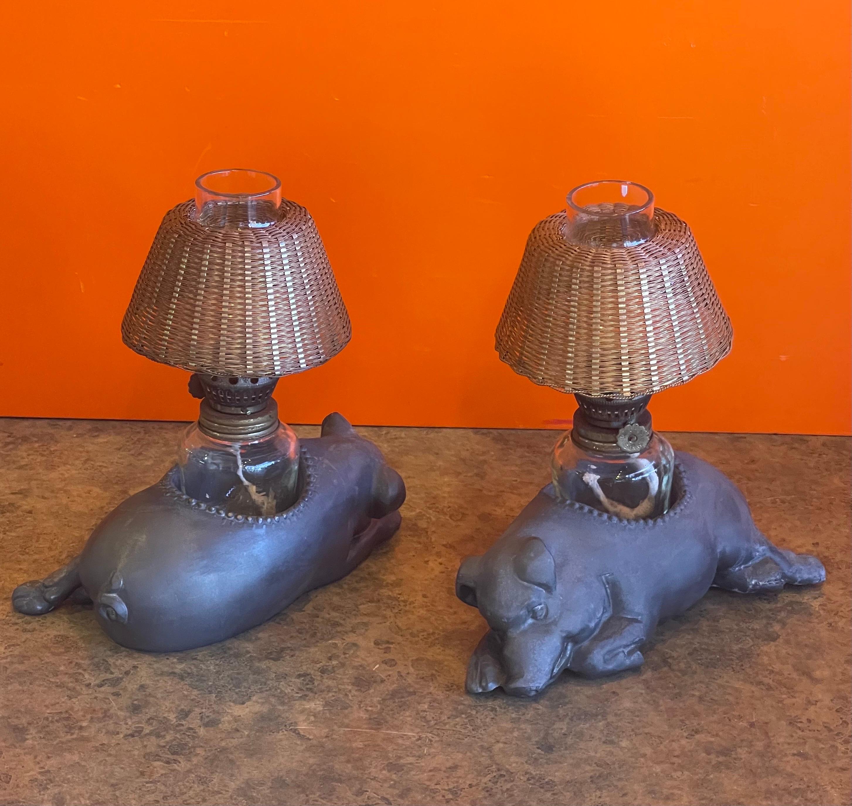 A very fun pair of vintage Morton's Steakhouse sleeping pig pewter oil lamps, circa 1980s. The lamps have graced Morton's tables since their first steakhouse opened in Chicago in 1978. Includes: Pewter pig figure, glass oil lamp and gold wicker
