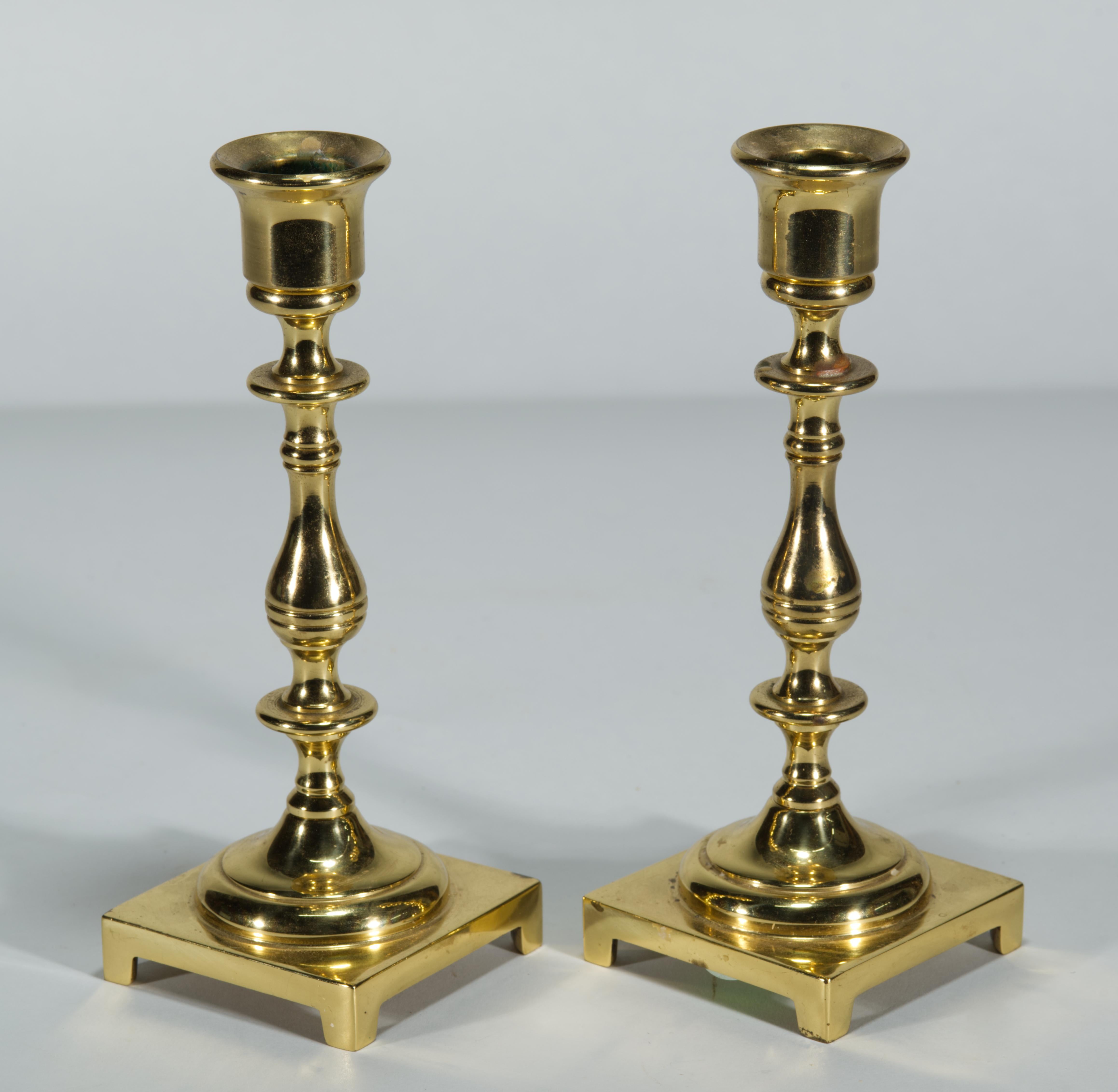 Paire de chandeliers balustres en laiton de style néoclassique présentant des colonnes finement détaillées reposant sur des bases carrées. Les bases à pied ajoutent de la définition aux corps sculptés et détaillés, couronnés de coupes de bougie