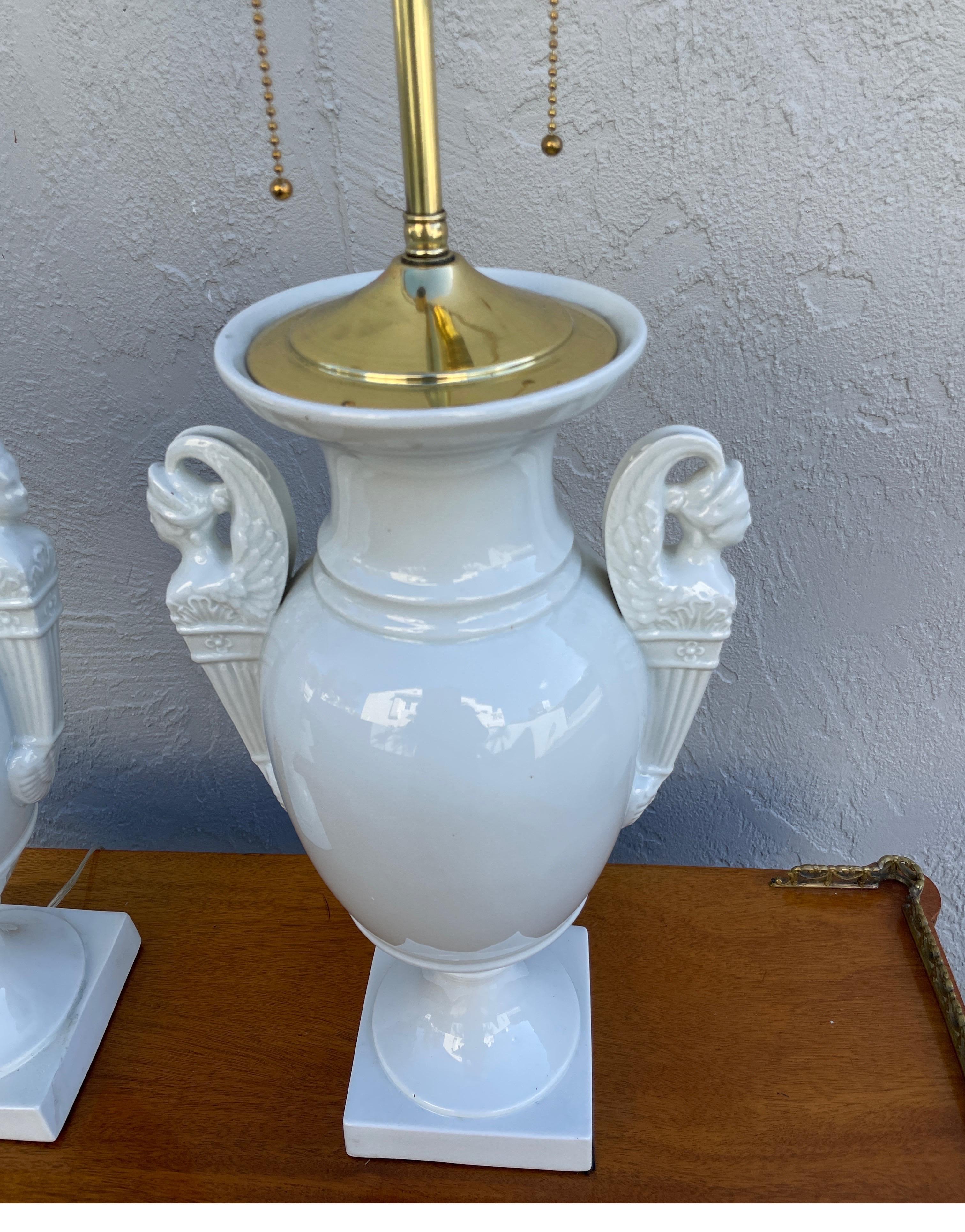 Pair of Vintage White Porcelain Neoclassical table lamps. Striking pair of Urn shaped lamps with figural handles. The top has a solid brass cap and sockets.