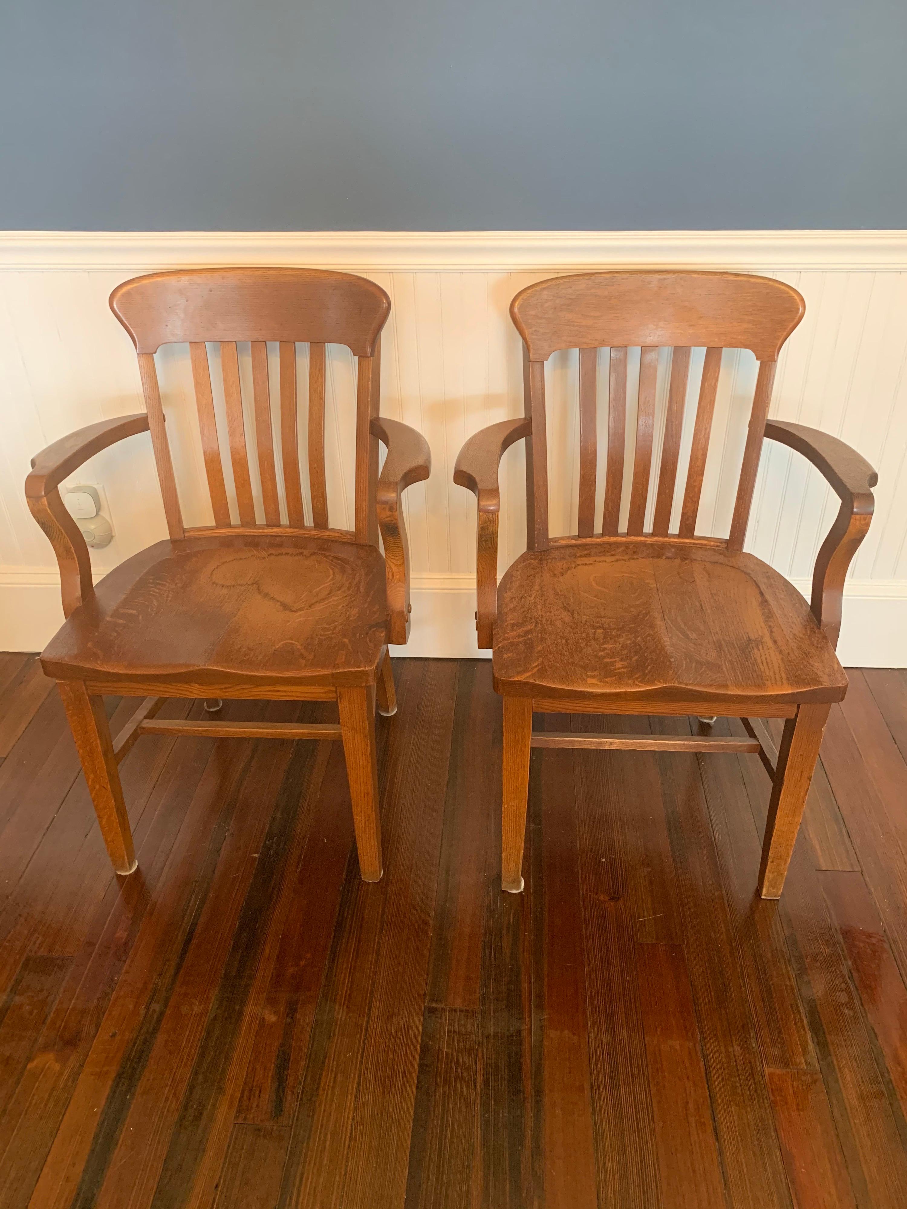 Pair of vintage oak Banker's or Barrister's armchairs.

These armchairs have a bannister styled backings ending in four simple tapered square legs. While the foundation of the chairs are quite standard the arms of the chairs have a beautiful and