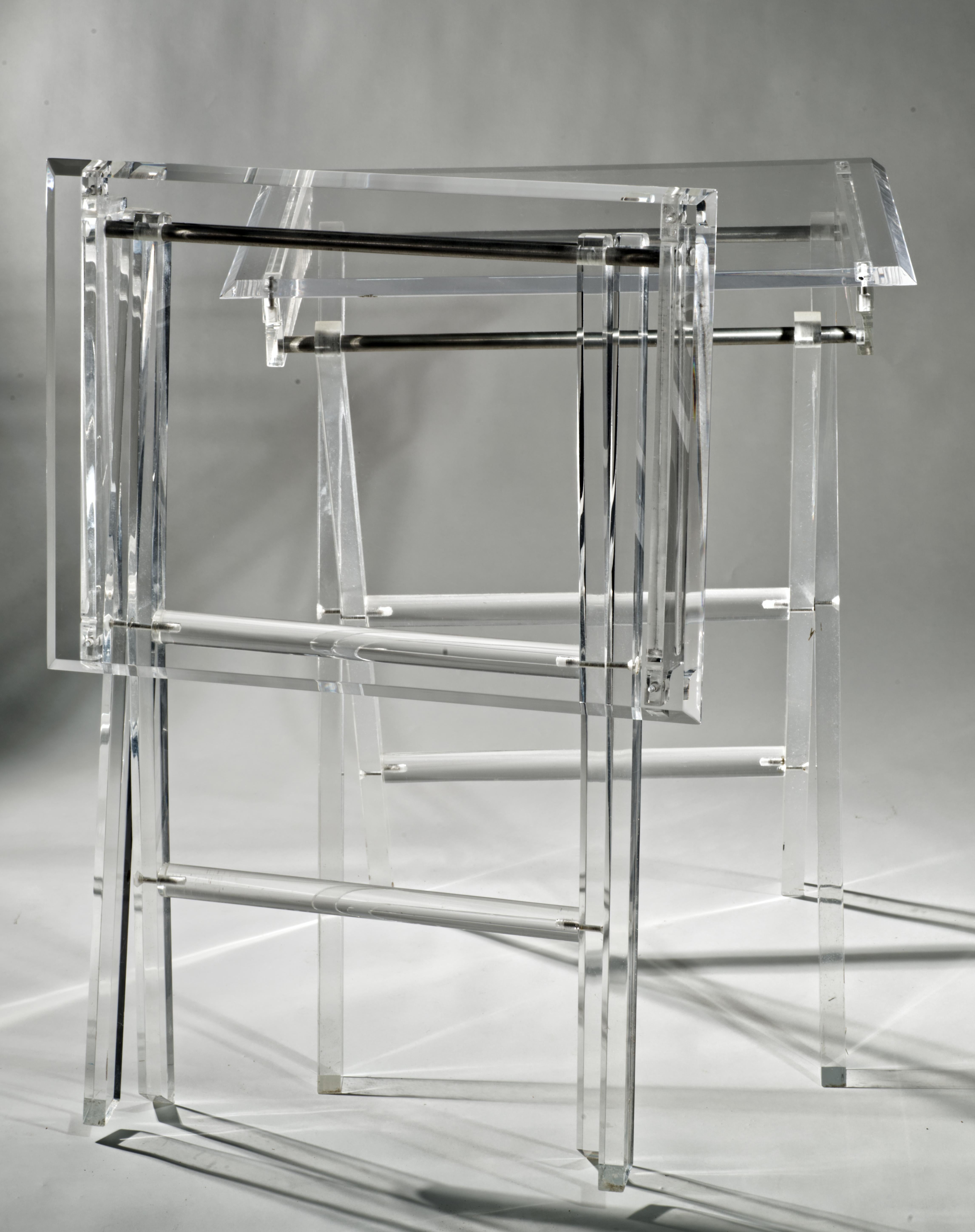  Beautiful set of two clear Lucite occasional tables features functional, streamlined folding design; the convenient shape allows the tables to be used as side tables or drinks tables next to sofa or chairs, or as serving trays or TV trays. 

Whie
