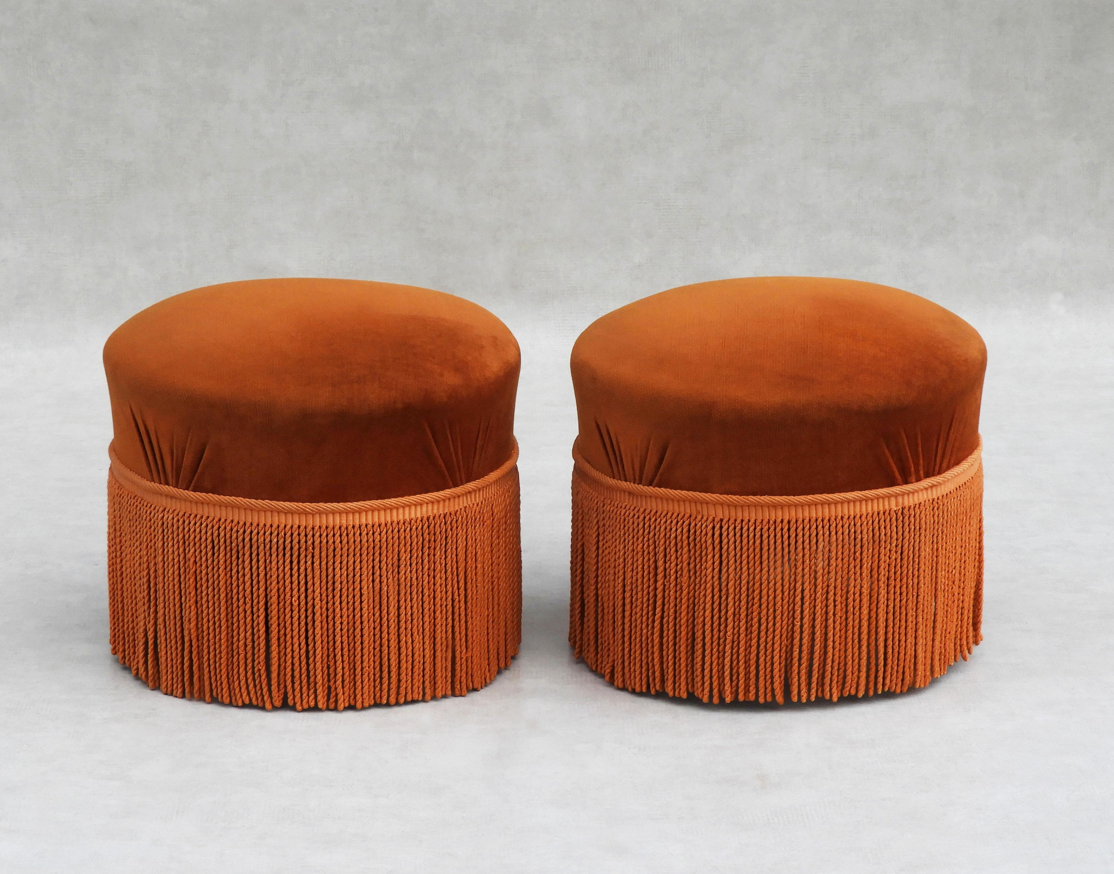 Gorgeous pair of mid-century French Ottomans.

Glamorous footstools in vibrant orange velvet velour trimmed with long floor-length fringe.
Round upholstered seat supported by four wooden legs.
All original upholstery in very good vintage
