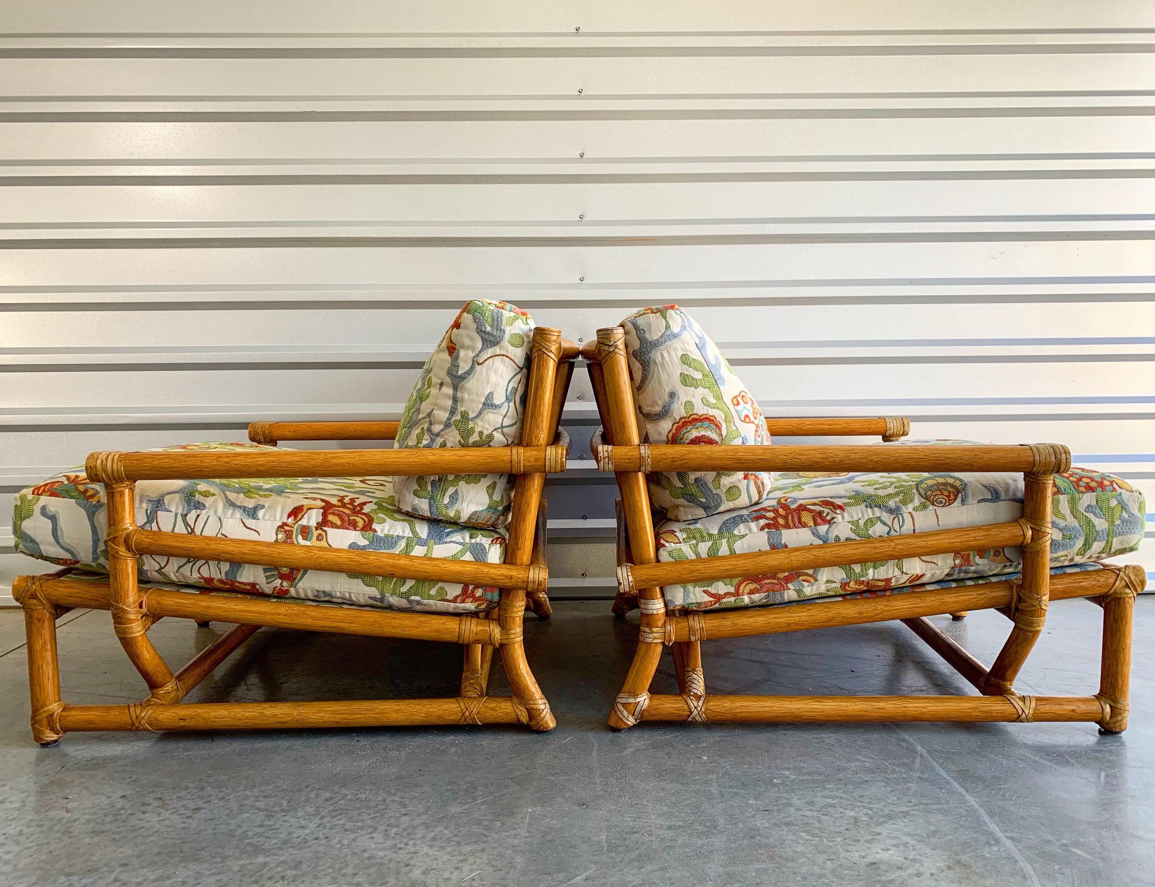Pair of substantial low slung bamboo rattan lounge chairs by McGuire. Built, circa 1970. Rawhide leather strapping joinery and end caps. Exquisite craftsmanship and top notch materials. Set includes two lounge chairs and one matching ottoman. Brass