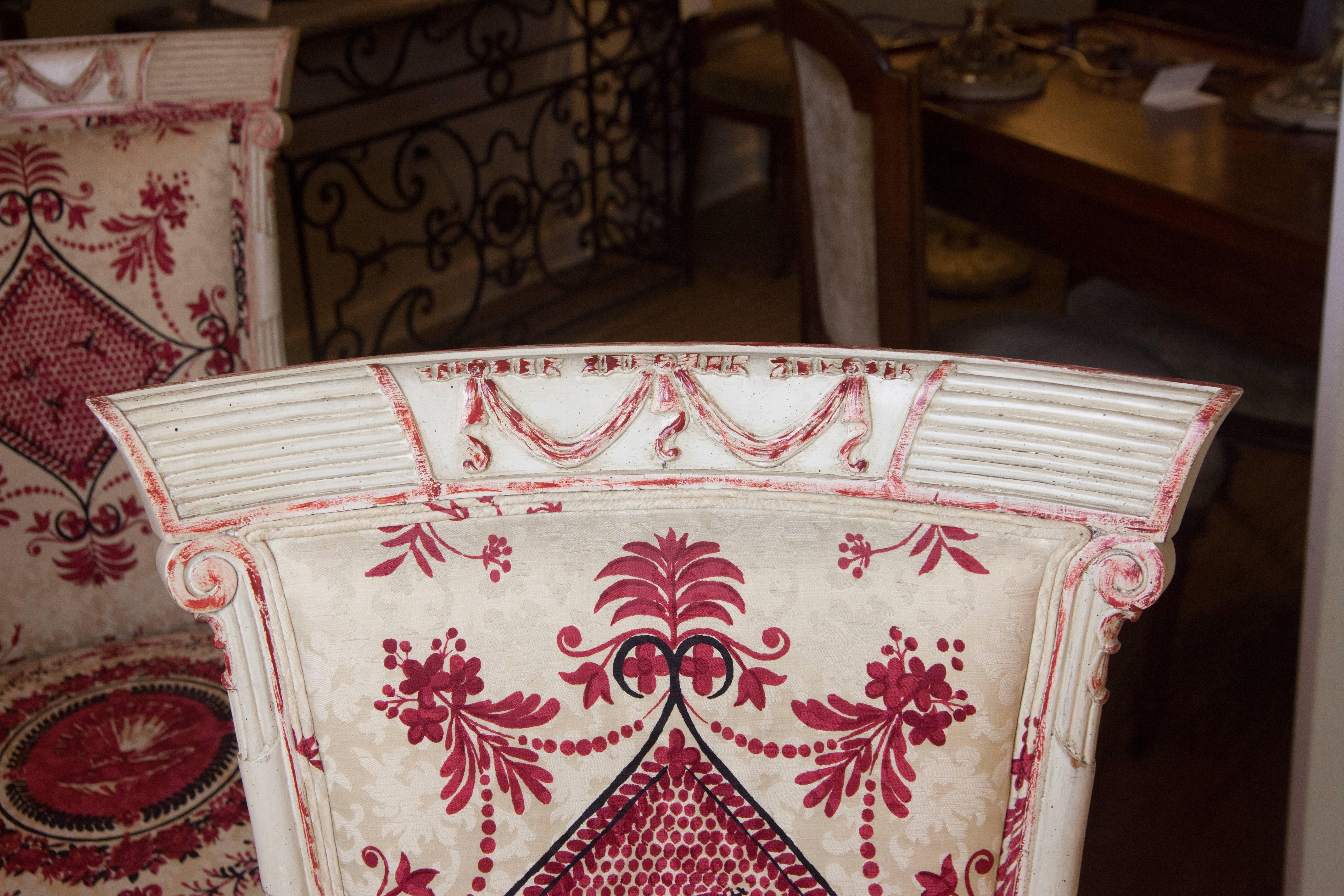This pair of vintage chinoiserie style armchairs has a faux cream finish with red accents. The chairs feature wood fluting with a lovely swag design on the chair back. The fabric is in excellent condition given it's age.