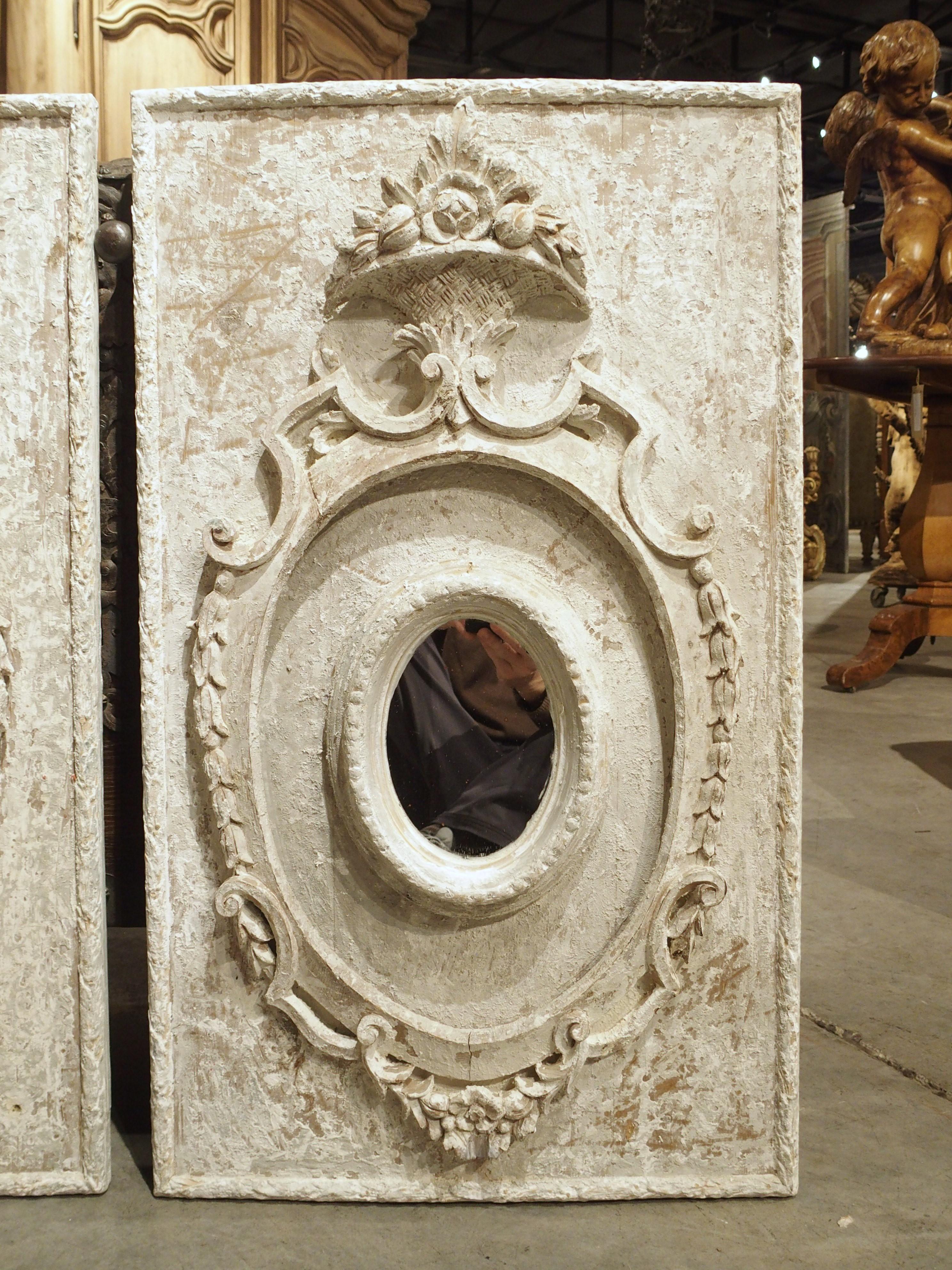 These painted panels were meticulously hand-crafted in Florence, Italy. The panels have been parcel-painted white with a 6 ¼ x 4 ½ oval mirror set inside an open cartouche. Both mirrors are surrounded by acanthus husks, floral swags, and volute