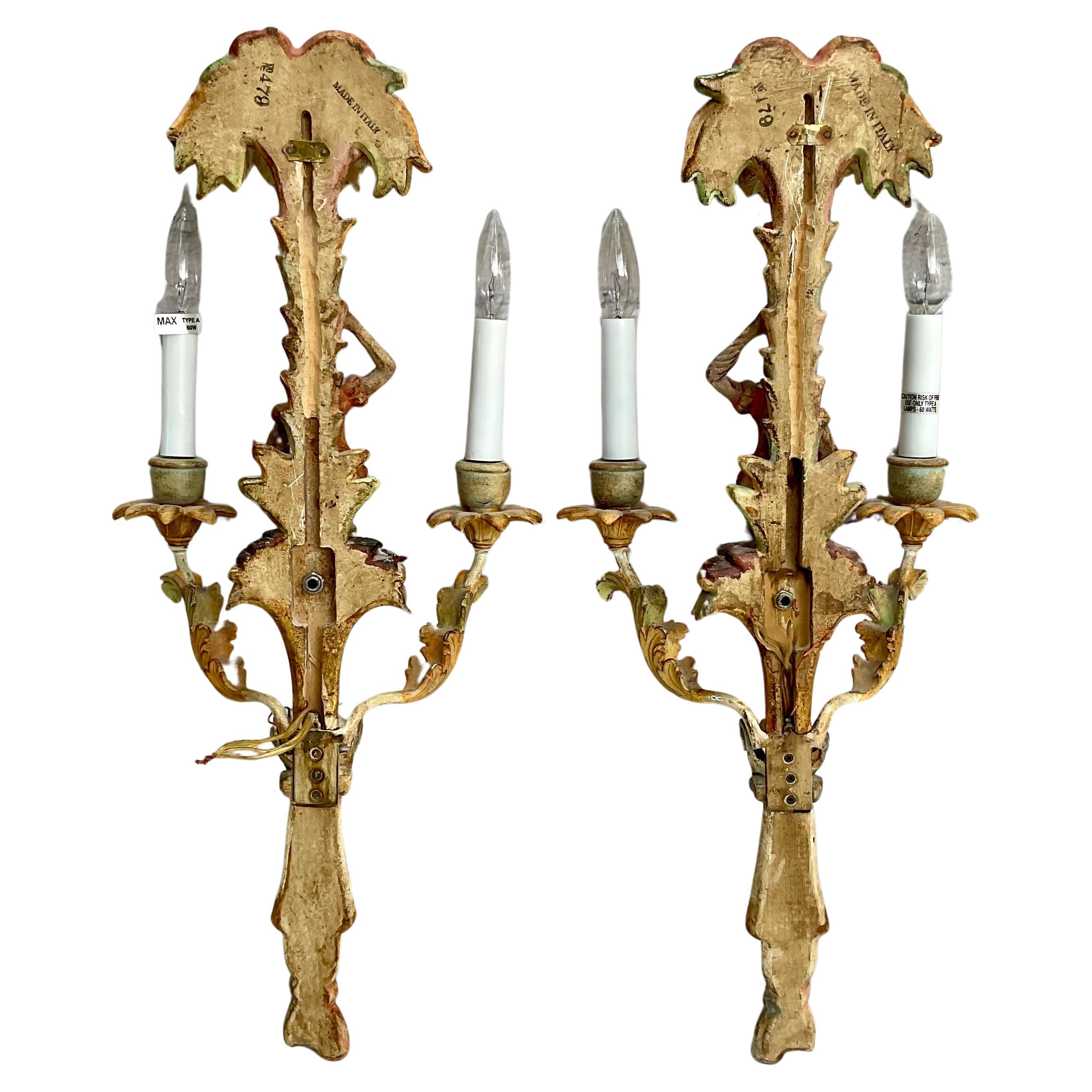 Pair of charming and whimsical vintage monkey wall sconces. Sconces feature beautifully painted palm-like tree with a painted monkey and two hard-wired lights on each sconce. Colors are in subtle red, blue, green and cream with gilt wood throughout.