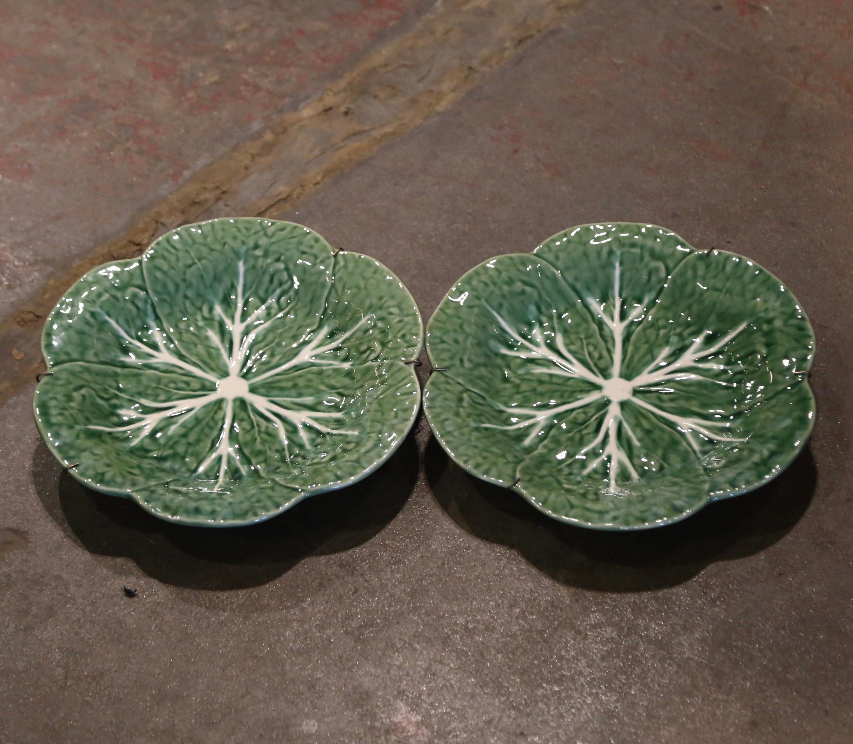 Decorate a wall or a shelf with this pair of antique wall plates. Crafted in portugal by Bordallo Pinheiro, each plate with scalloped rim features a cabbage form center in the green and beige palette. Both pieces are in excellent condition with rich