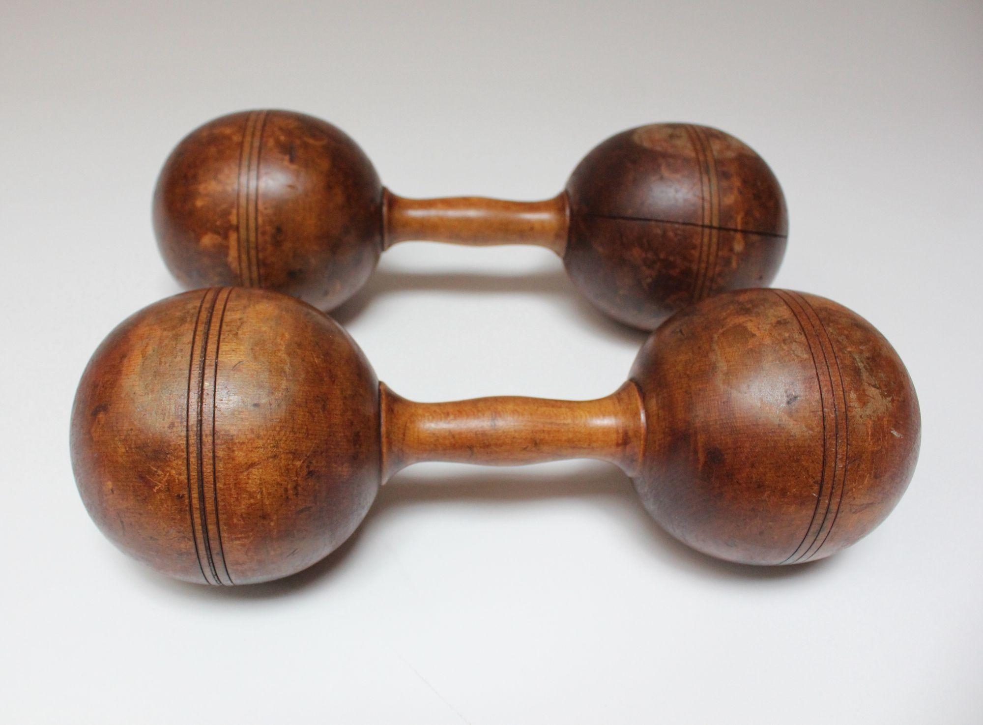 Hand-carved dumbbells, each from one continuous piece of wood accented with carved lines (circa 1930s, USA).
Natural toned wood, perfectly aged with rich patina/soiling/splits from age and use. Beautiful tabletop decorative objets d'art.
Relatively