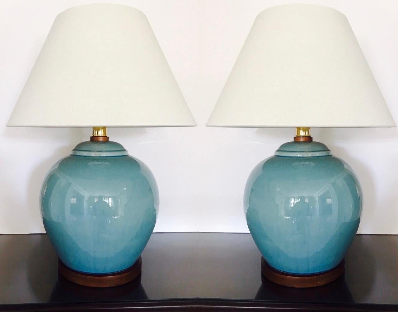 Gorgeous pair of large ceramic pottery lamps in Robin's Egg Blue. The lamps feature a crackle glaze finish with hand-painted trim in cerulean blue and with walnut wood bases and fittings. Fitted with brass sockets and three-way switch and shown with