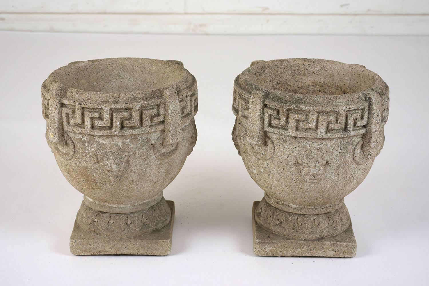 This pair of 1950s Regency style planters are made from concrete with a natural finish. The planters have a classic urn shape with a Greek meander key band along the top and faint impressions of grape bunches along the sides and acanthus leaves at